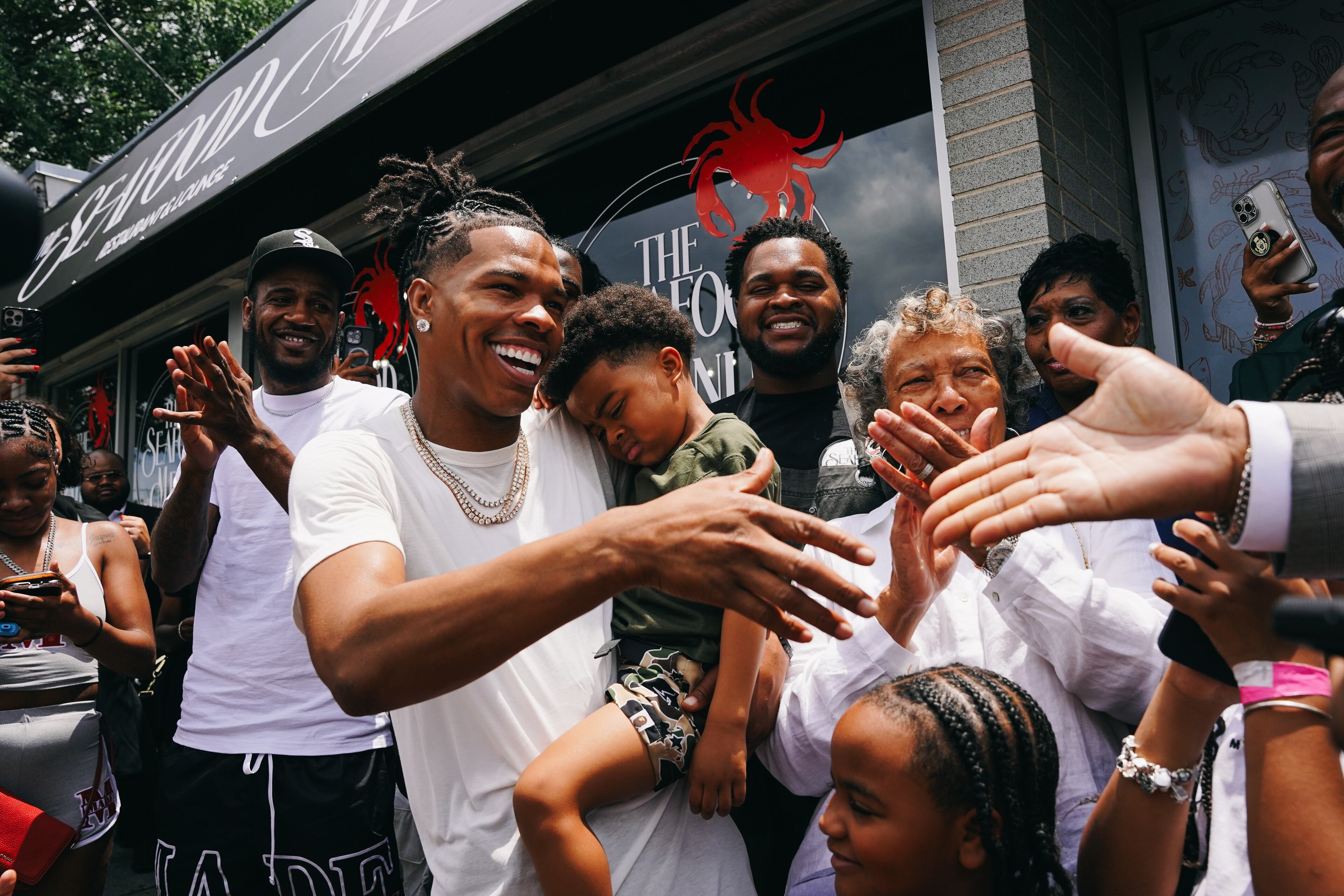 Rapper Lil Baby (center) holds his son, Loyal, as he shakes hands with City Councilman Byron Amos at the grand opening of his restautant, the Seafood Menu, in Atlanta, Georgia on Friday, July 14, 2023. (Olivia Bowdoin / Atlanta Journal-Constitution)