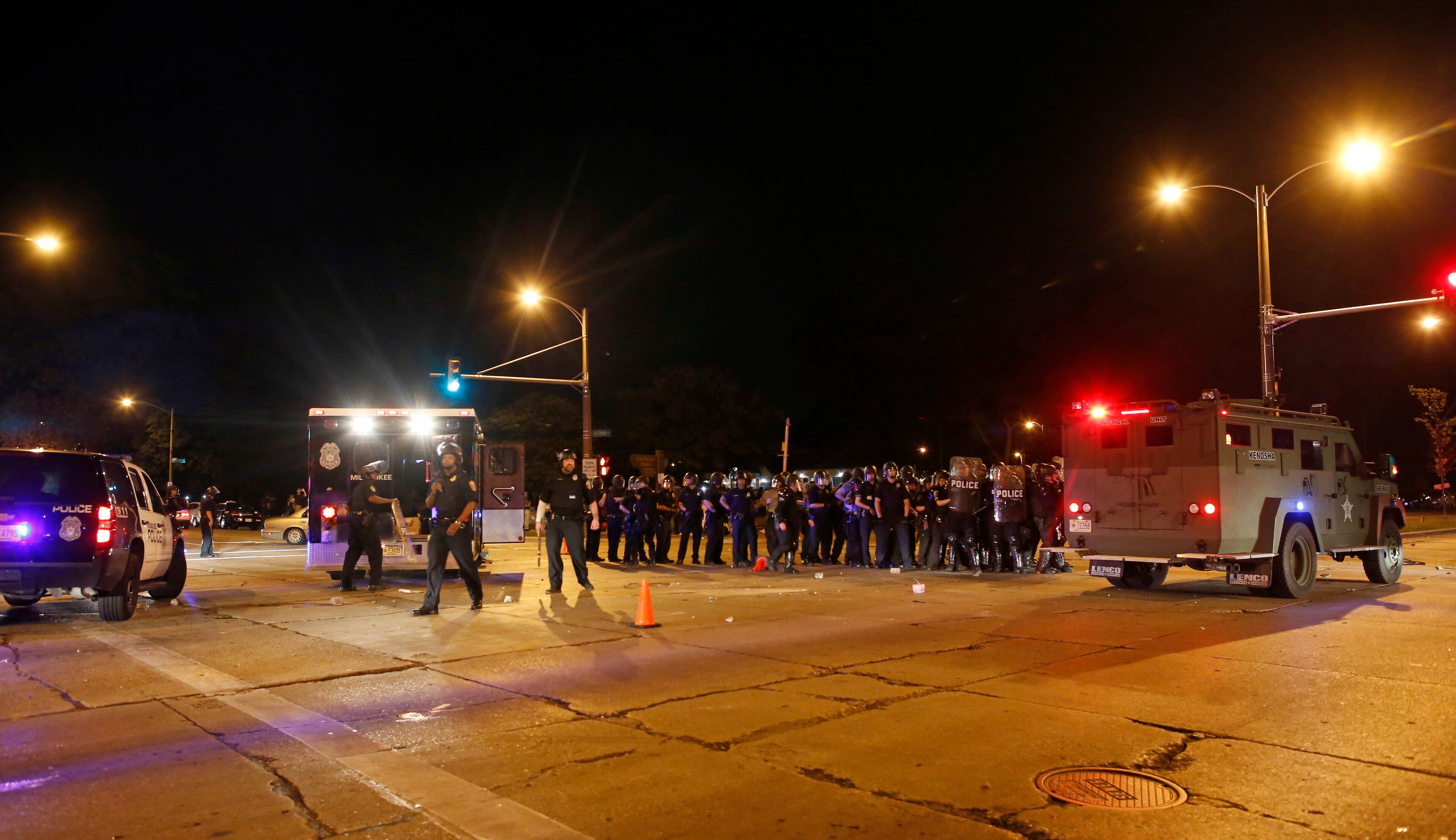 Police hide behind an armored vehicle as rocks are hurled at them in Milwaukee, Sunday, Aug. 14, 2016. Police said one person was shot at a Milwaukee protest on Sunday evening and officers used an armored vehicle to retrieve the injured victim during a second night of unrest over the police shooting of a black man, but there was no repeat of widespread destruction of property. Some two dozen officers in riot gear confronted a group who were throwing rocks and other objects at police near where the black man was fatally shot a day earlier. (AP Photo/Jeffrey Phelps)