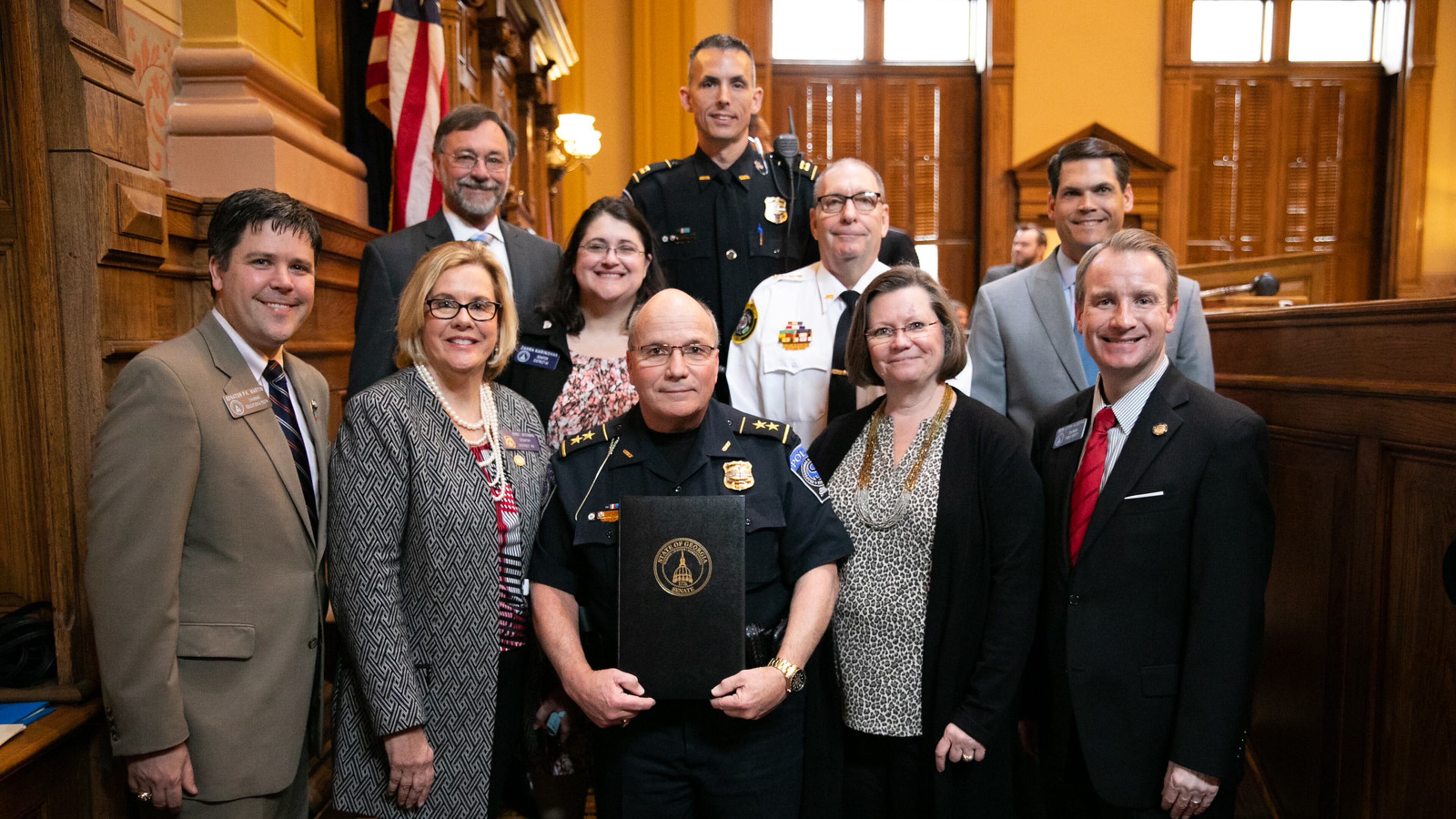 Suwanee Police Chief Mike Jones was recently honored at the State Capitol as Georgia’s 2018-2019 Chief of the Year. Top row: Suwanee Police Captain Cass Mooney; Second row, left to right: Suwanee Mayor Jimmy Burnette, Senator Zahra Karinshak, President of the Georgia Association of Chiefs of Police and City of Jefferson Chief Joe Wirthman , Georgia Lieutenant Governor Geoff Duncan; Bottom row, left to right: Senator PK Martin, Senator Renee Unterman, Chief Mike Jones, Mrs. Debbie Anne Jones, Senator John Albers. (Courtesy City of Suwanee)