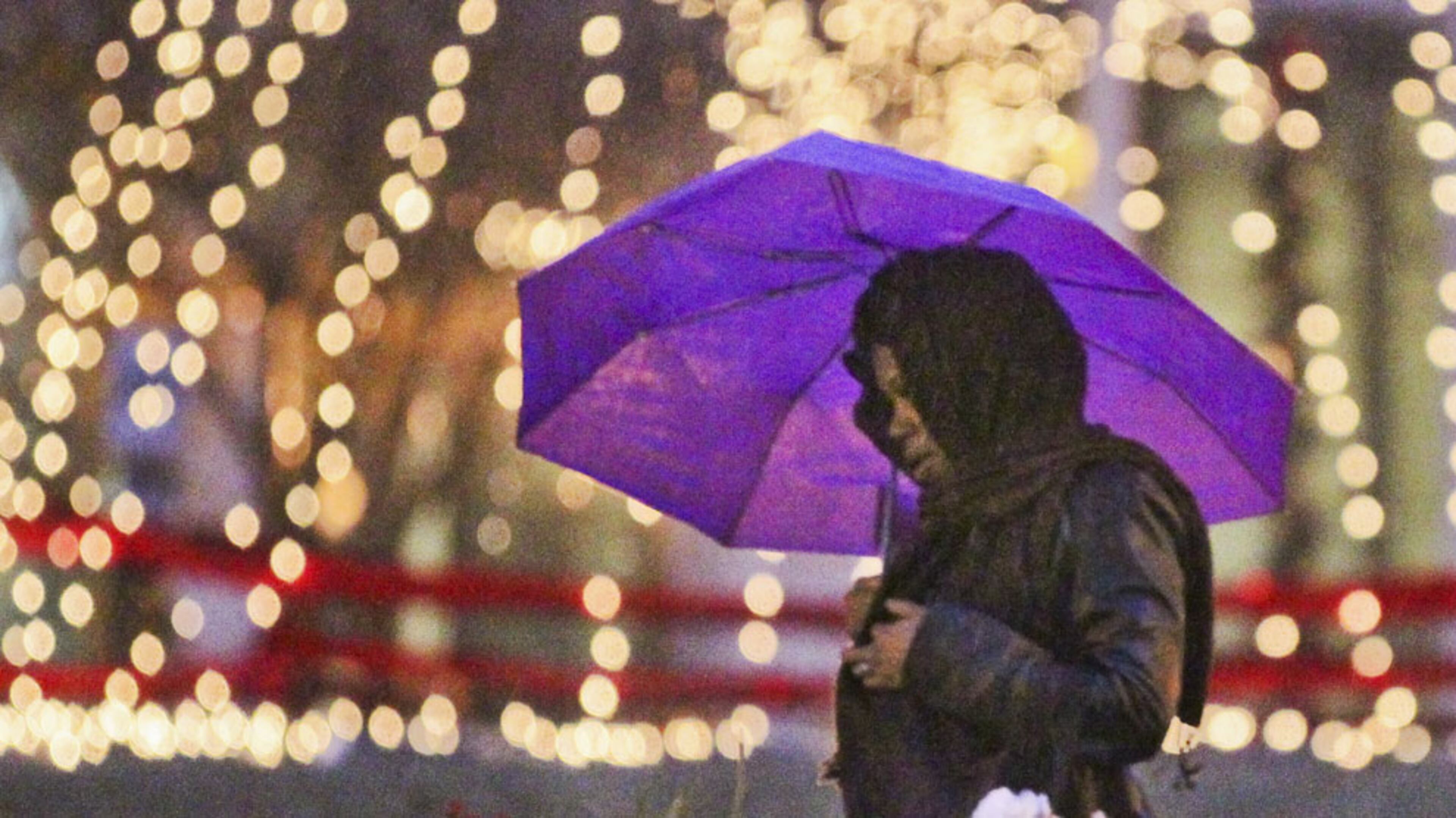 Zelda Perkins walks along Peachtree Street in the rain Thursday morning near the Christmas lights of Woodruff Park.