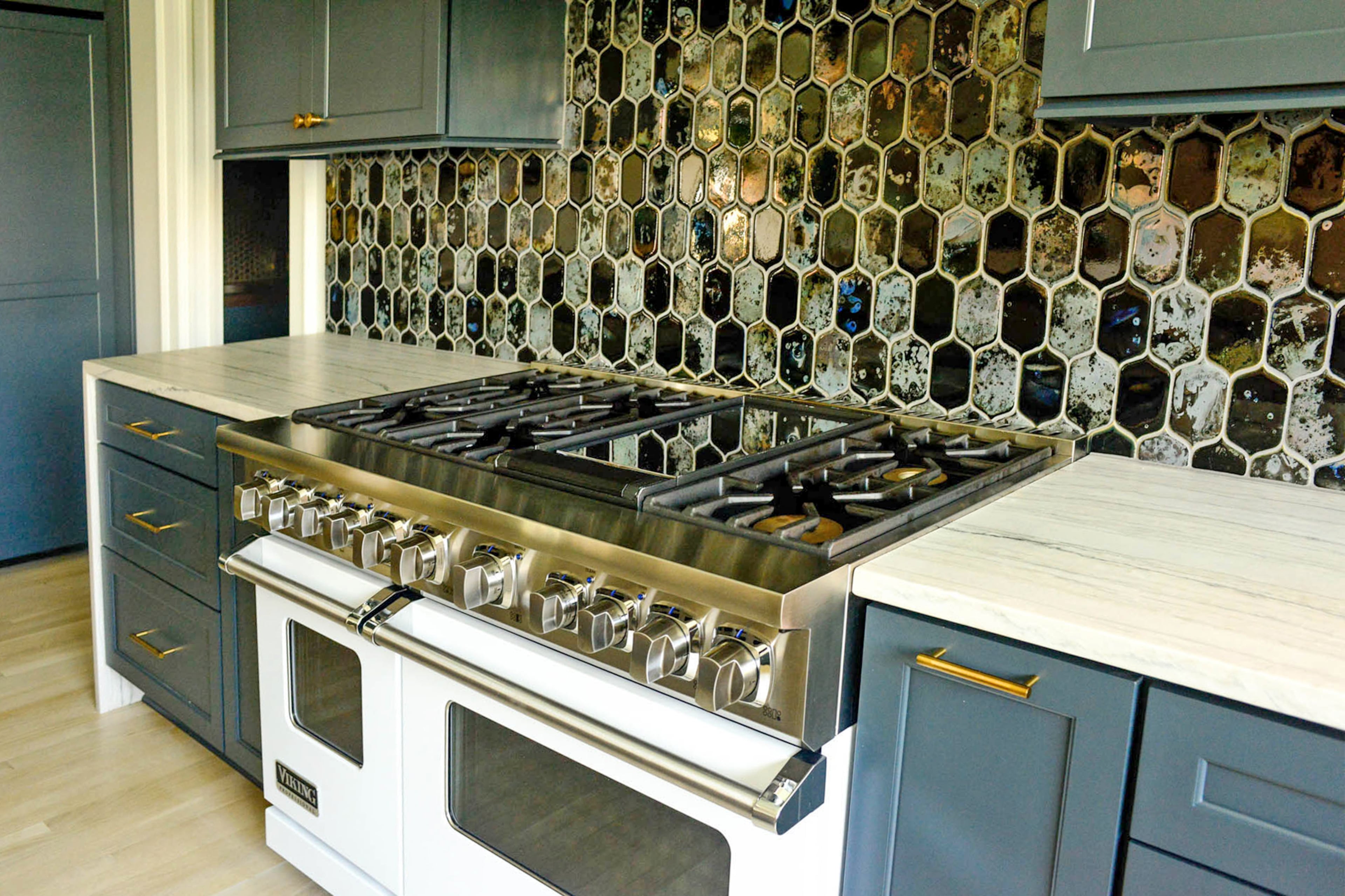 The kitchen has a number of striking elements, including a white professional-grade Viking range, blue cabinetry and a white-and-gray countertop in a waterfall style. The iridescent backsplash tile contains blues, grays and gold.