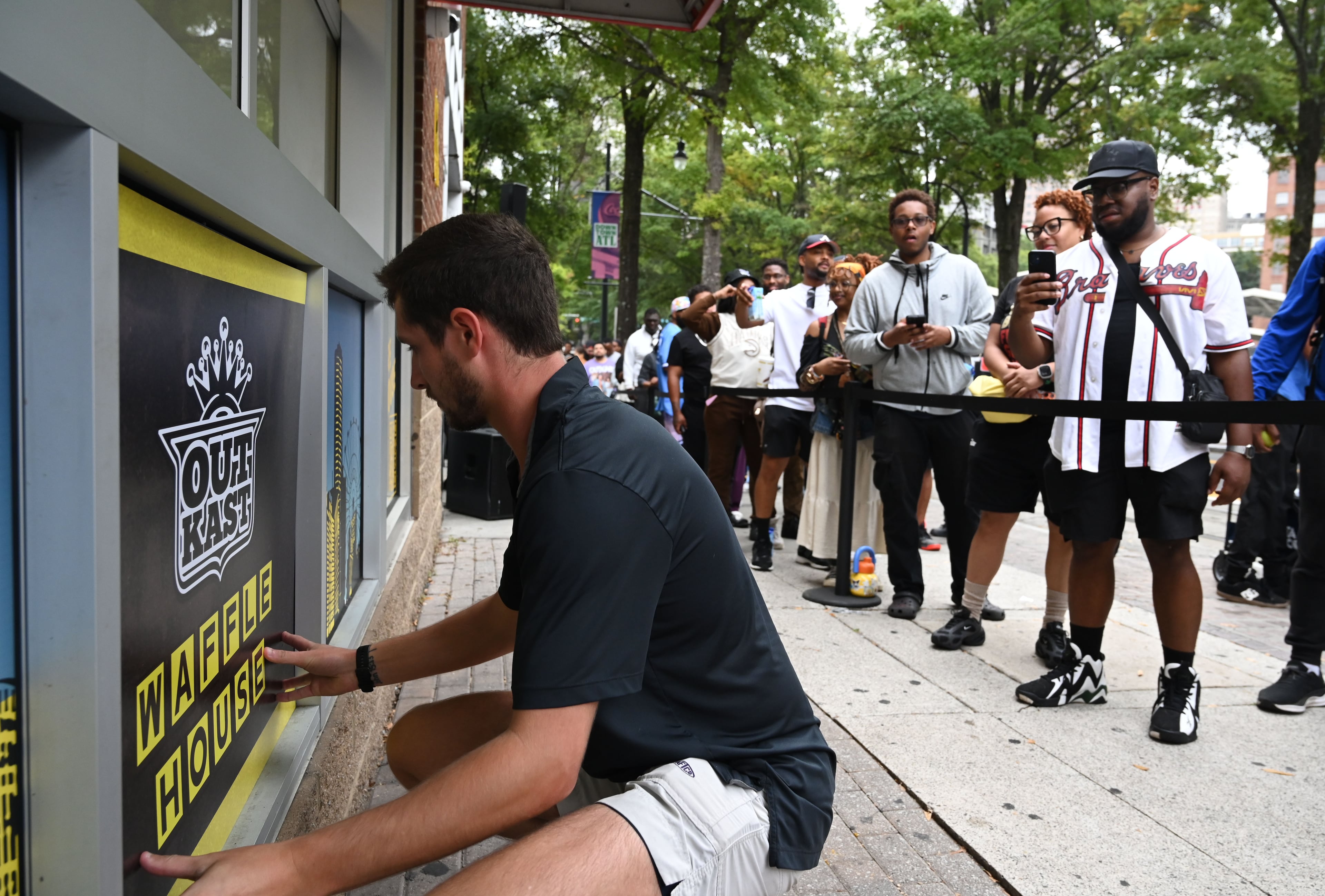 An event staff member places signs as people wait for the pop-up store to open. (Hyosub Shin/AJC)