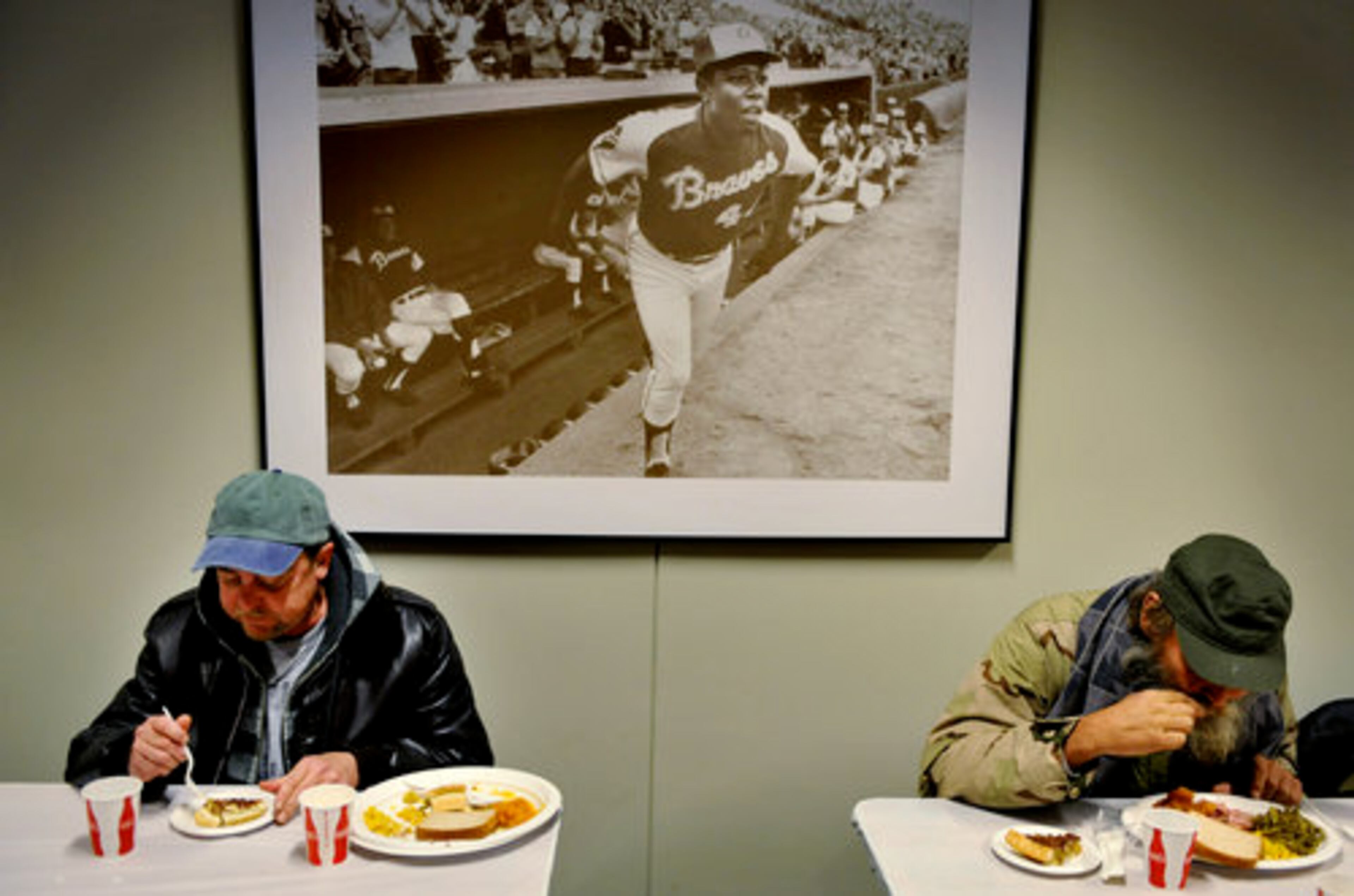 David Dunlap and Chris Youngs, both of whom are homeless, eat below a large picture of Hall-of-Famer and former Braves player Hank Aaron. Hosea Feed The Hungry and Homeless was founded in 1971 by civil right leader Rev. Hosea Williams.