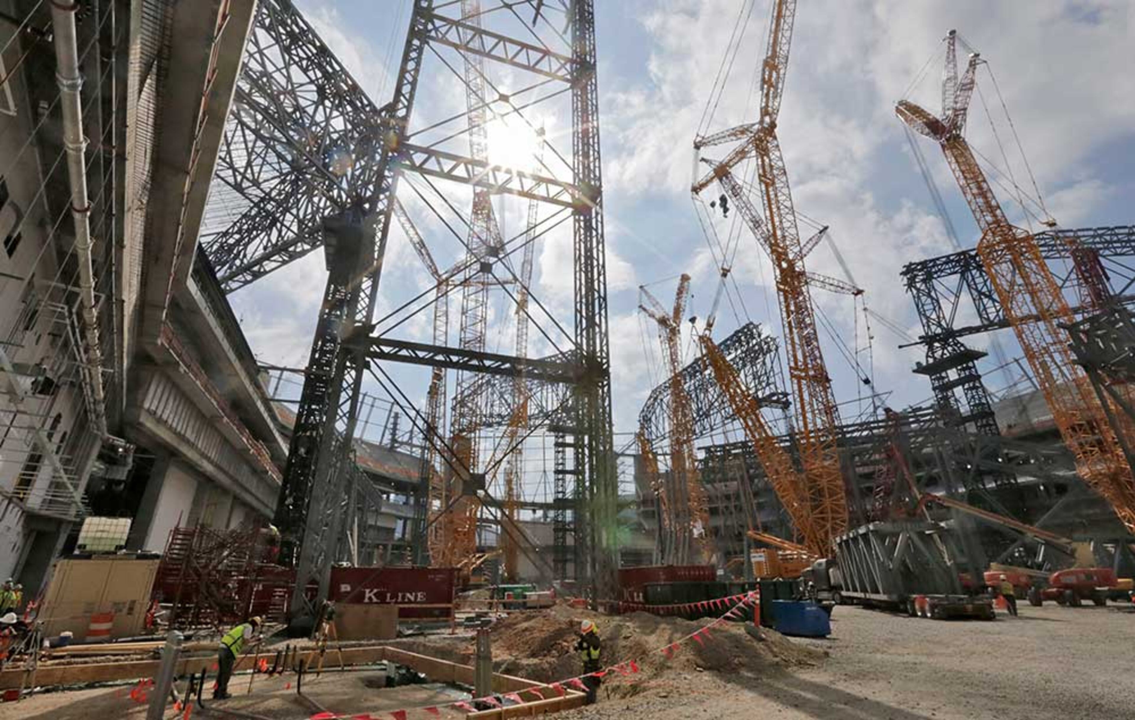 The field level is filled with steel work and cranes as tower construction and roof steel truss ground assembly continues inside the bowl.