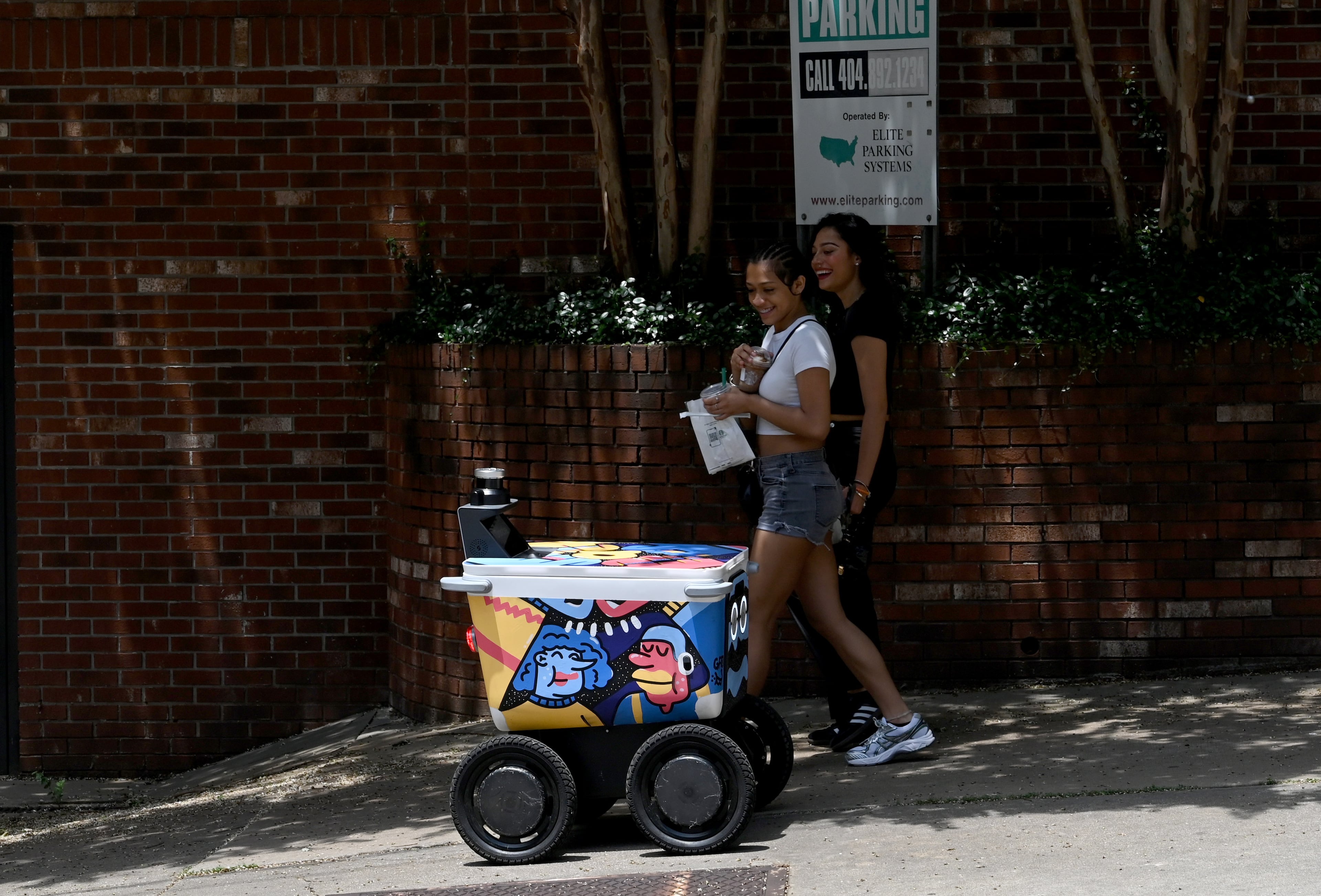 Pedestrians react as a food delivery robot “Darcie” made by Serve Robotics makes a demo delivery in midtown, Thursday, June 26, 2025, in Atlanta. The robot was painted by Atlanta muralist George F. Baker III. (Hyosub Shin/AJC)