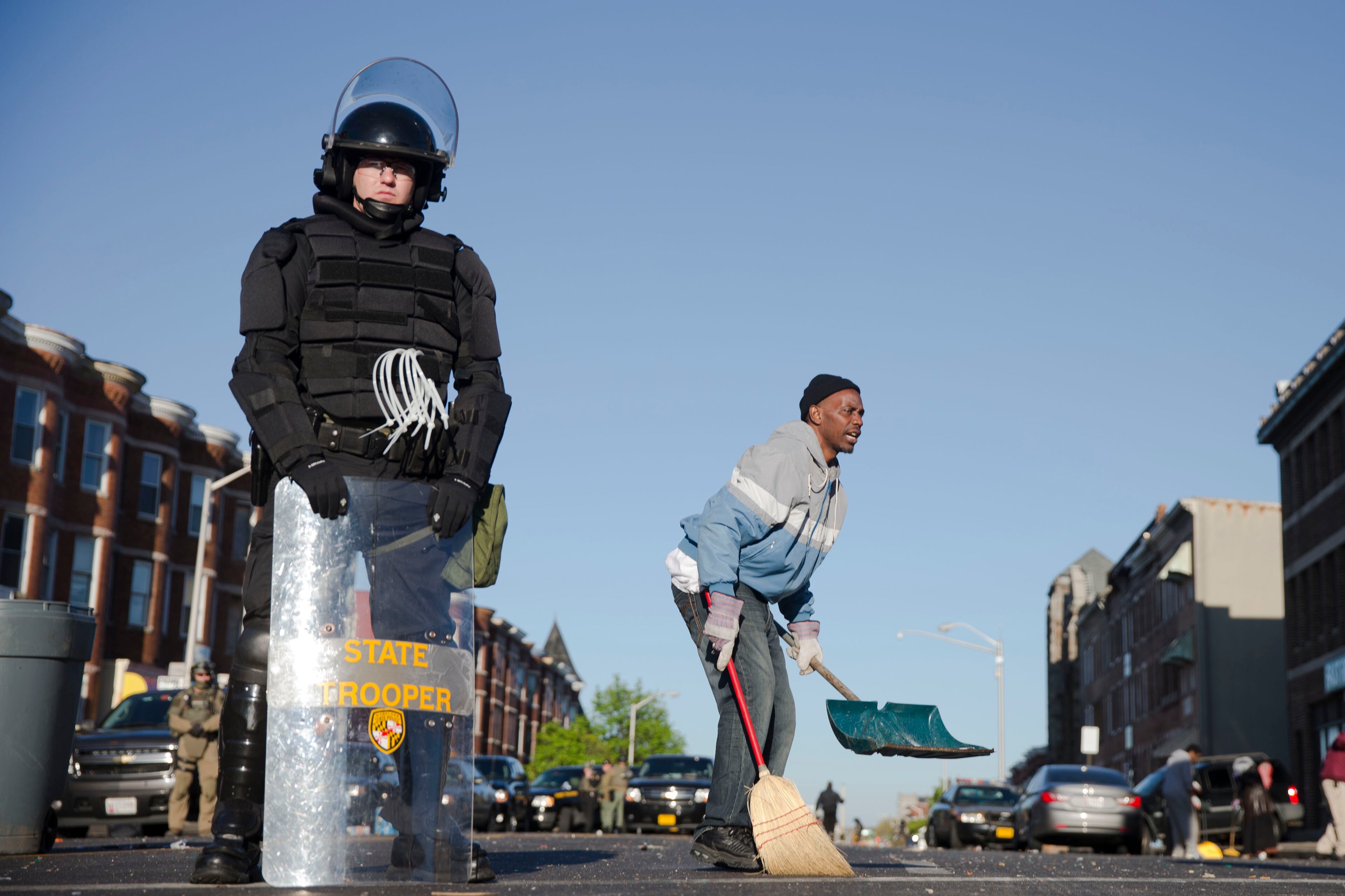 Residents clean streets as law enforcement officers stand guard, Tuesday, April 28, 2015, in Baltimore, in the aftermath of rioting following Monday's funeral of Freddie Gray, who died in police custody. (AP Photo/Matt Rourke)
