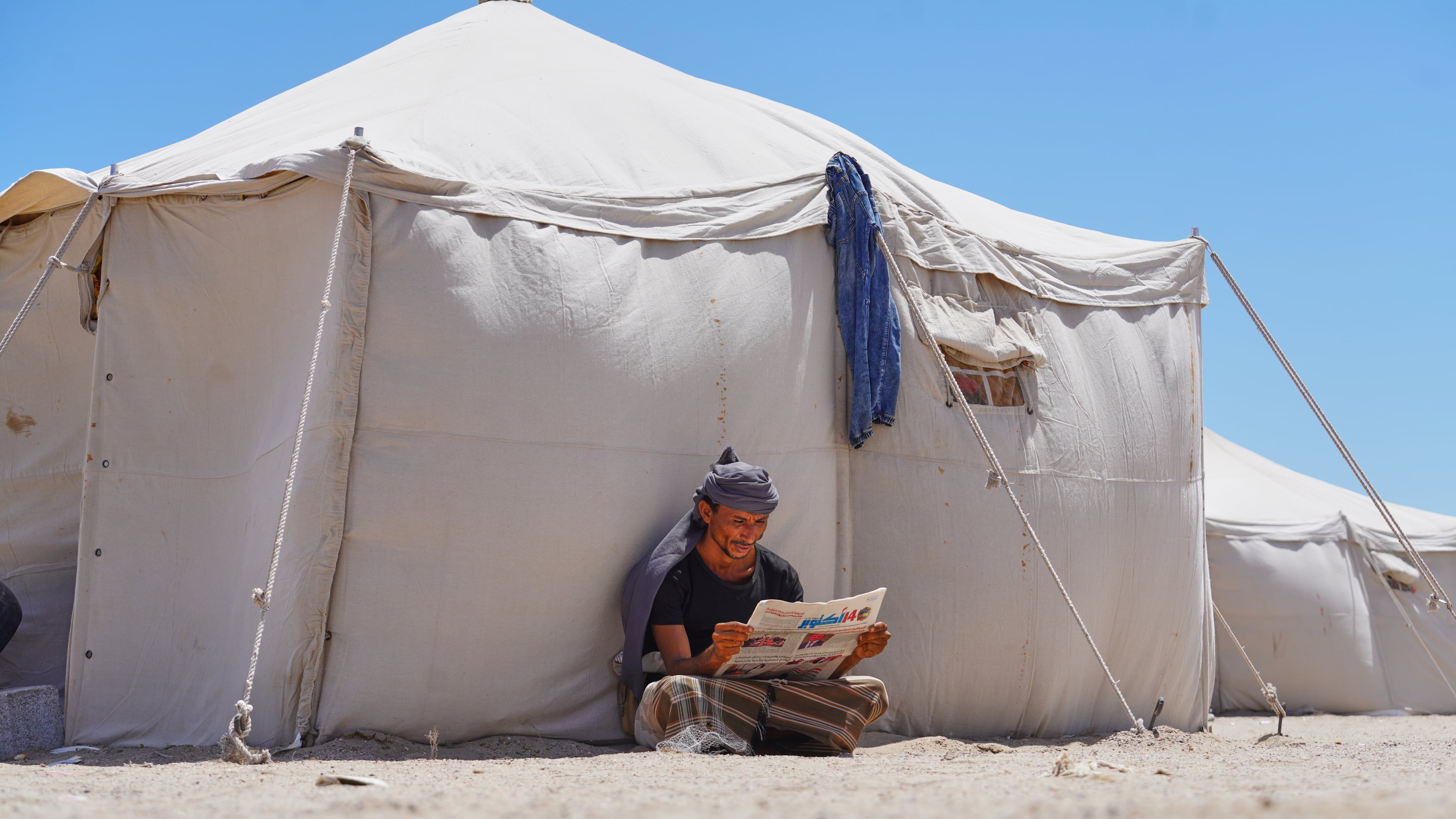 A displaced Yemeni reads a newspaper at the Al-Firdaws camp in Ras Imran on the western outskirts of Aden, Yemen, Monday, Oct. 5, 2026. (AP Photo/Abdulnasser Alseddik)