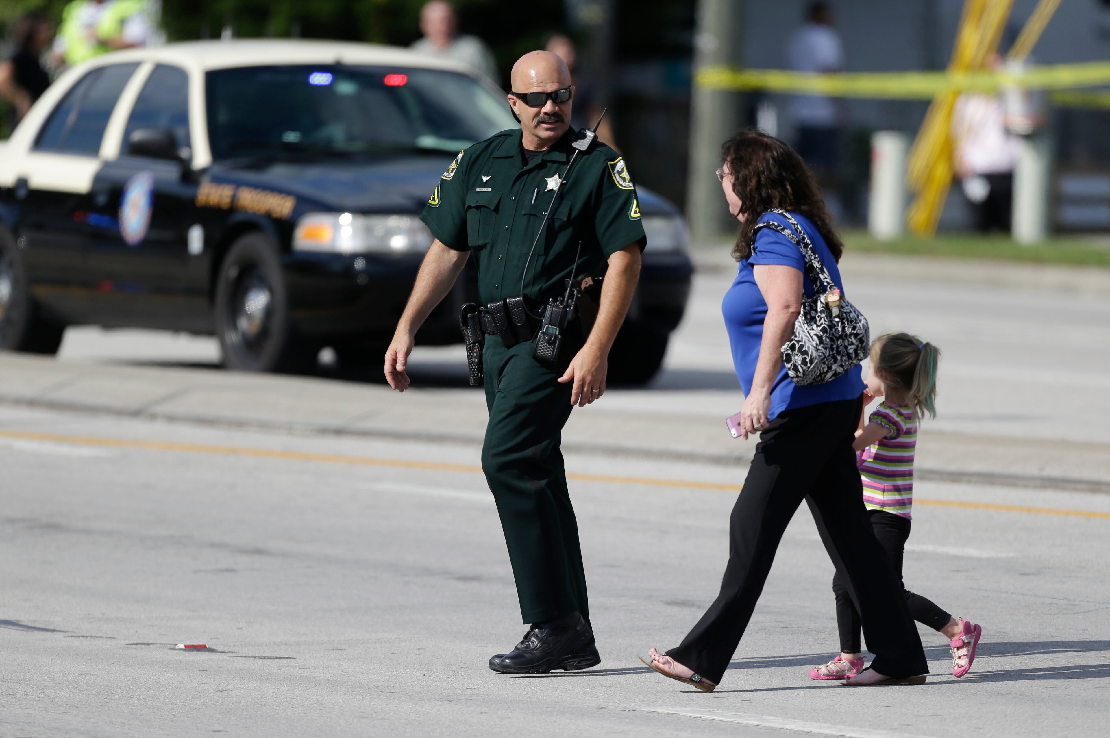 An Orange County Sheriff's deputy, left, escorts a mother and her child across a street after a vehicle crashed into a day care center, Wednesday, April 9, 2014, in Winter Park, Fla. (AP Photo/John Raoux)
