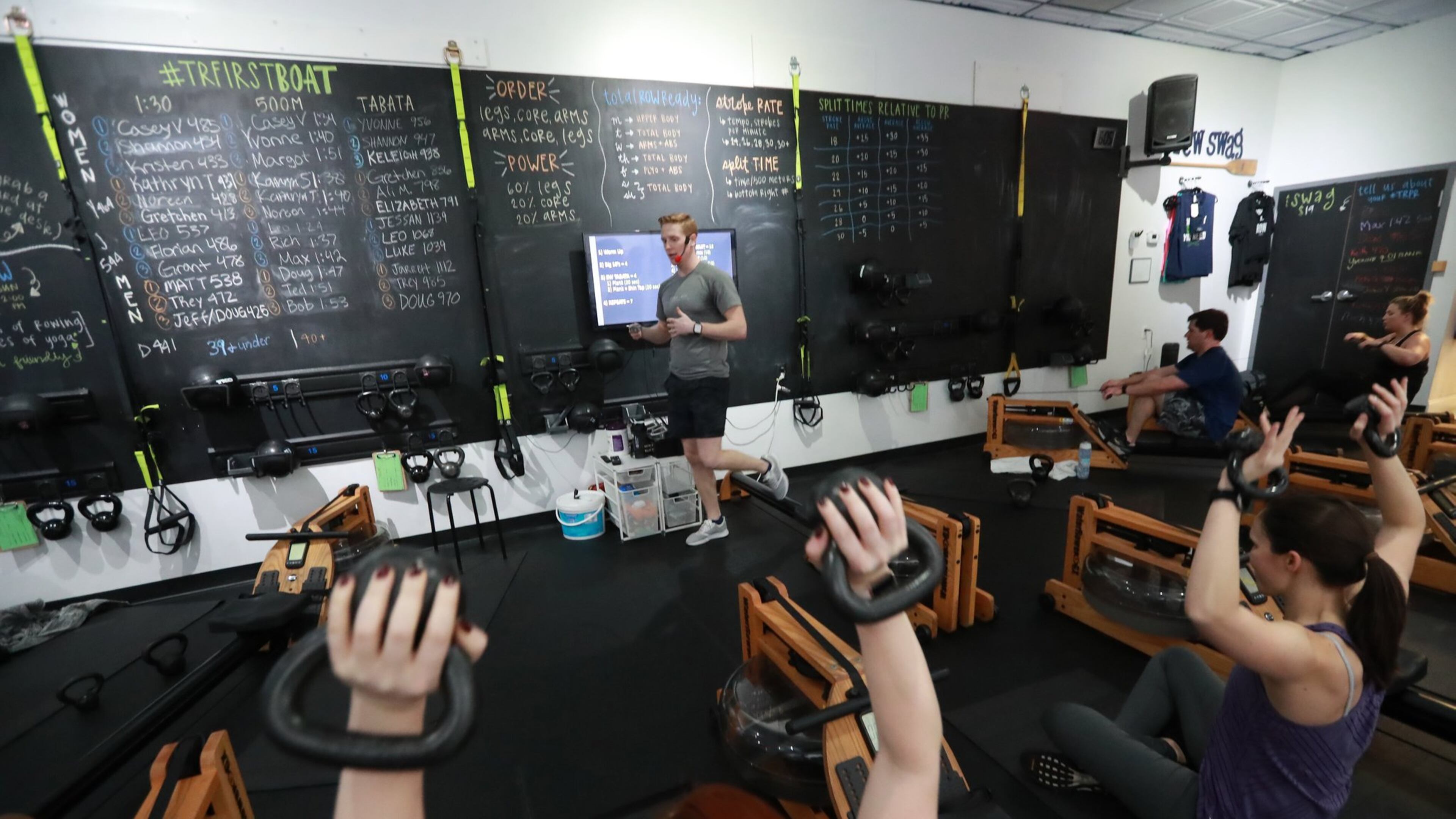Dylan Loope, a trainer at Total Row Fitness, leads a fitness class on rowing machines in Atlanta. Loope pieces together a living from multiple part-time trainer jobs. Curtis Compton ccompton@ajc.com