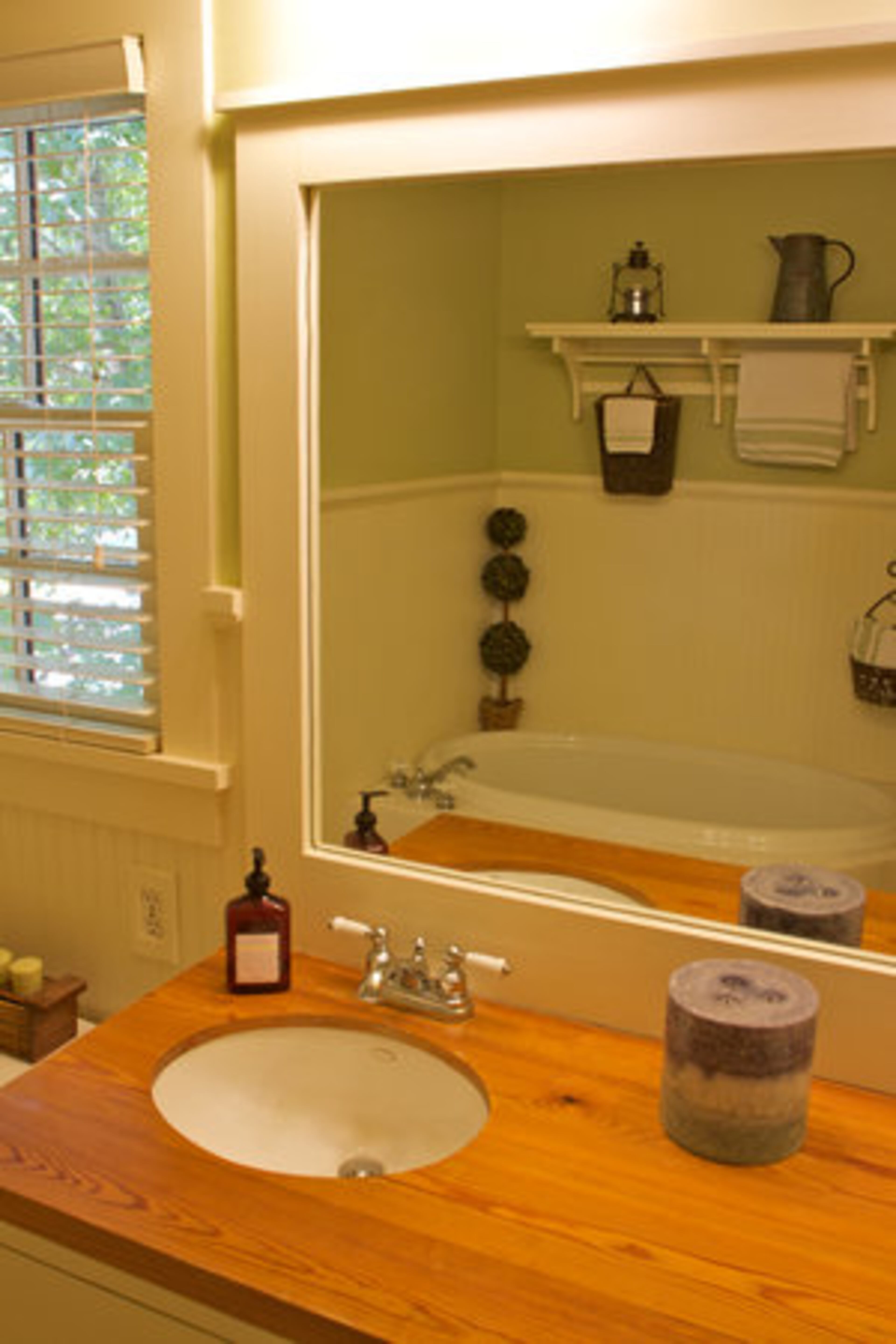 The same reclaimed heart pine countertops found in the kitchen are also present in Todd and Laura Strickland's master bathroom. The room features a whirlpool tub and white wainscoting with green accent color.