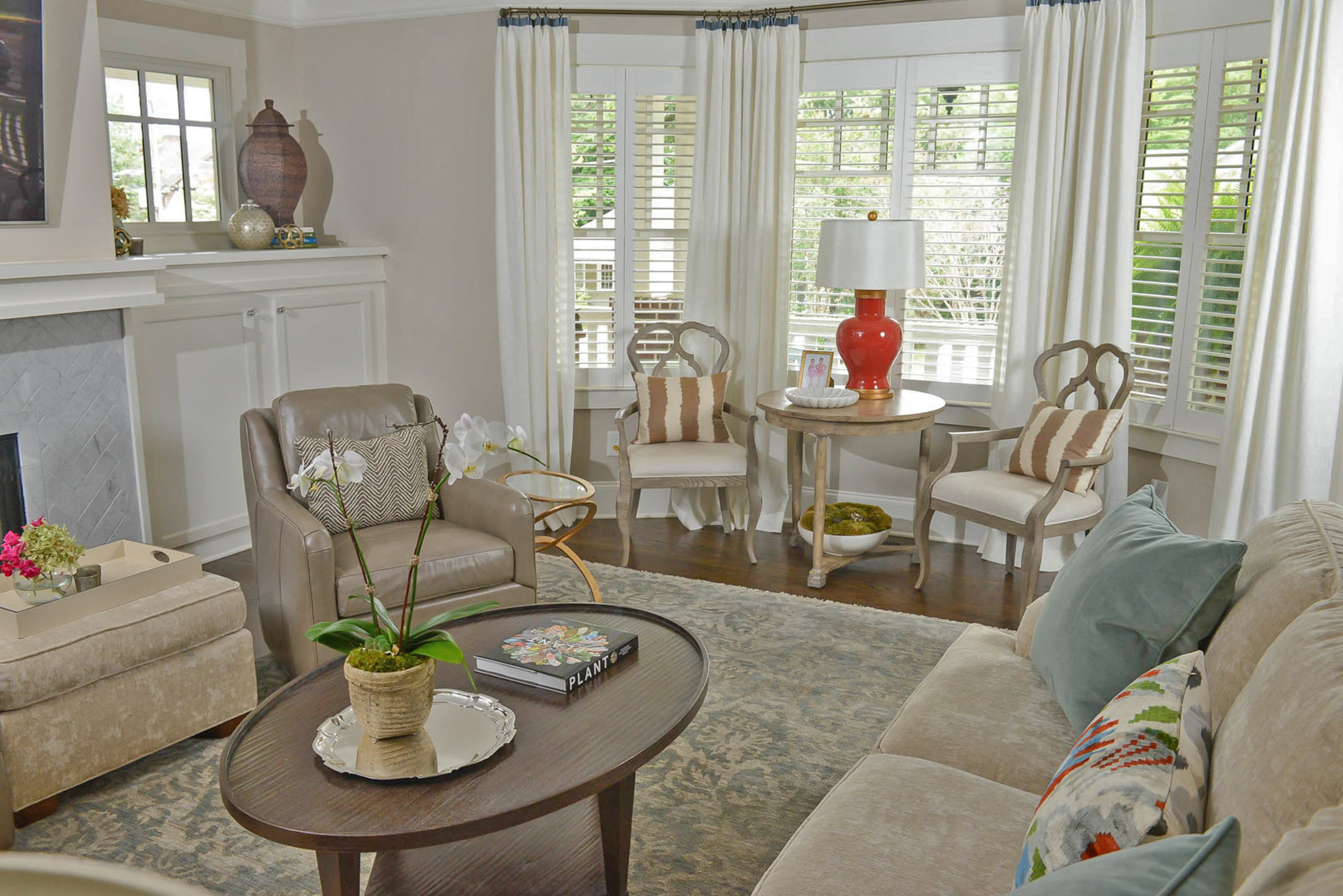 A tea table from Vanguard Furniture topped with a red lamp from Bradburn Home and wooden chairs by Bernhardt are nestled into the window of the bungalow. Other seating areas in the living room include leather swivel chairs from Vanguard with custom pillows made of Vervain fabric. Kate loves finding artwork at the Decatur Arts Festival, which is where she found the glazed ceramics by North Carolina artist Brenna McBroom that now flank the fireplace.