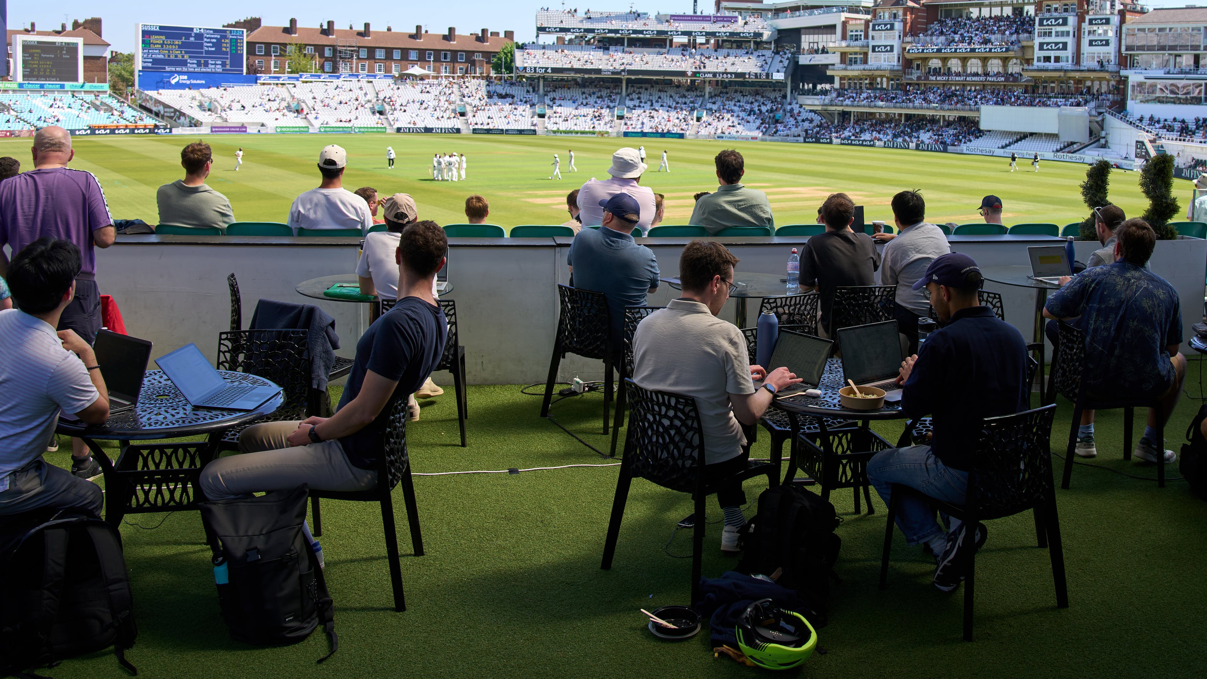 People work and watch cricket during a Surrey against Sussex County Championship cricket match at the Kia Oval in London, Friday, May 1, 2026. (AP Photo/Tony Hicks)