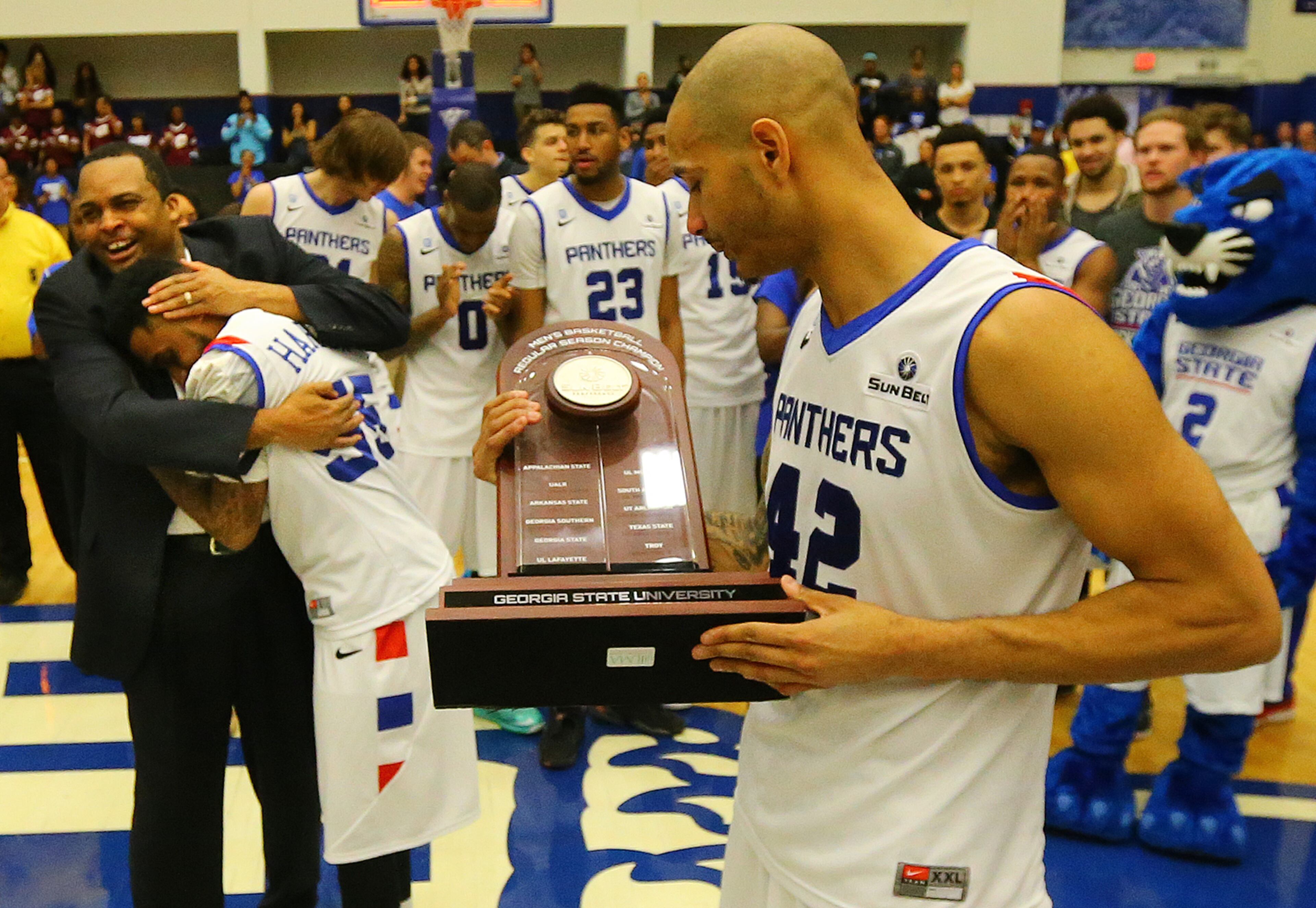 Georgia State forward Curtis Washington holds the Sun Belt men's basketball regular season championship trophy as head coach Ron Hunter embraces guard Ryan Harrow after beating Georgia Southern 72-55 in a basketball game on Saturday, March 7, 2015, in Atlanta.
