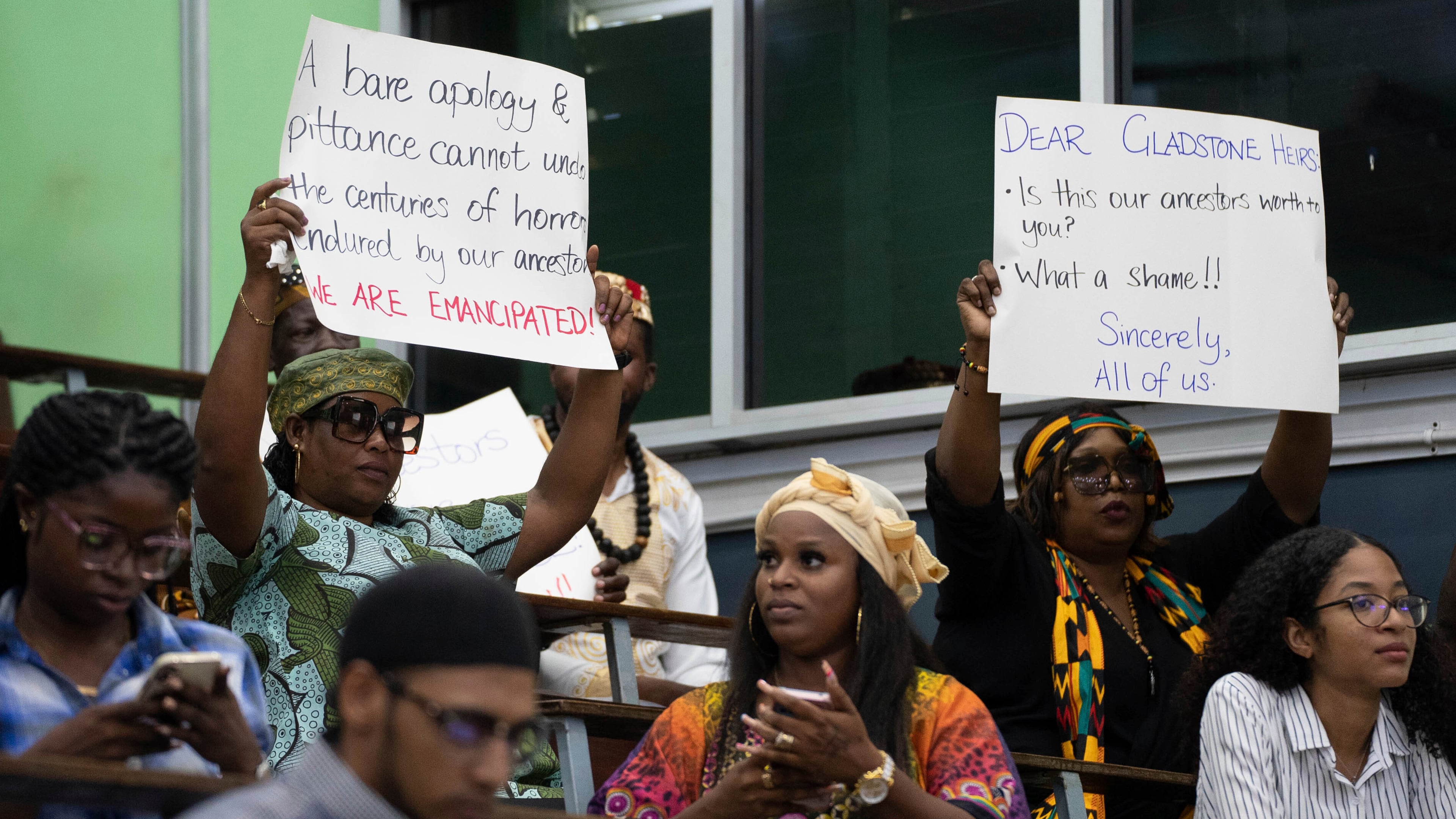 FILE - People hold signs during a speech by Charles Gladstone, a descendant of former plantation owner John Gladstone, as he delivers an apology on behalf of the Gladstone family at Georgetown University in Georgetown, Guyana, Friday, Aug. 25, 2023. (AP Photo/Chris Leung, File)