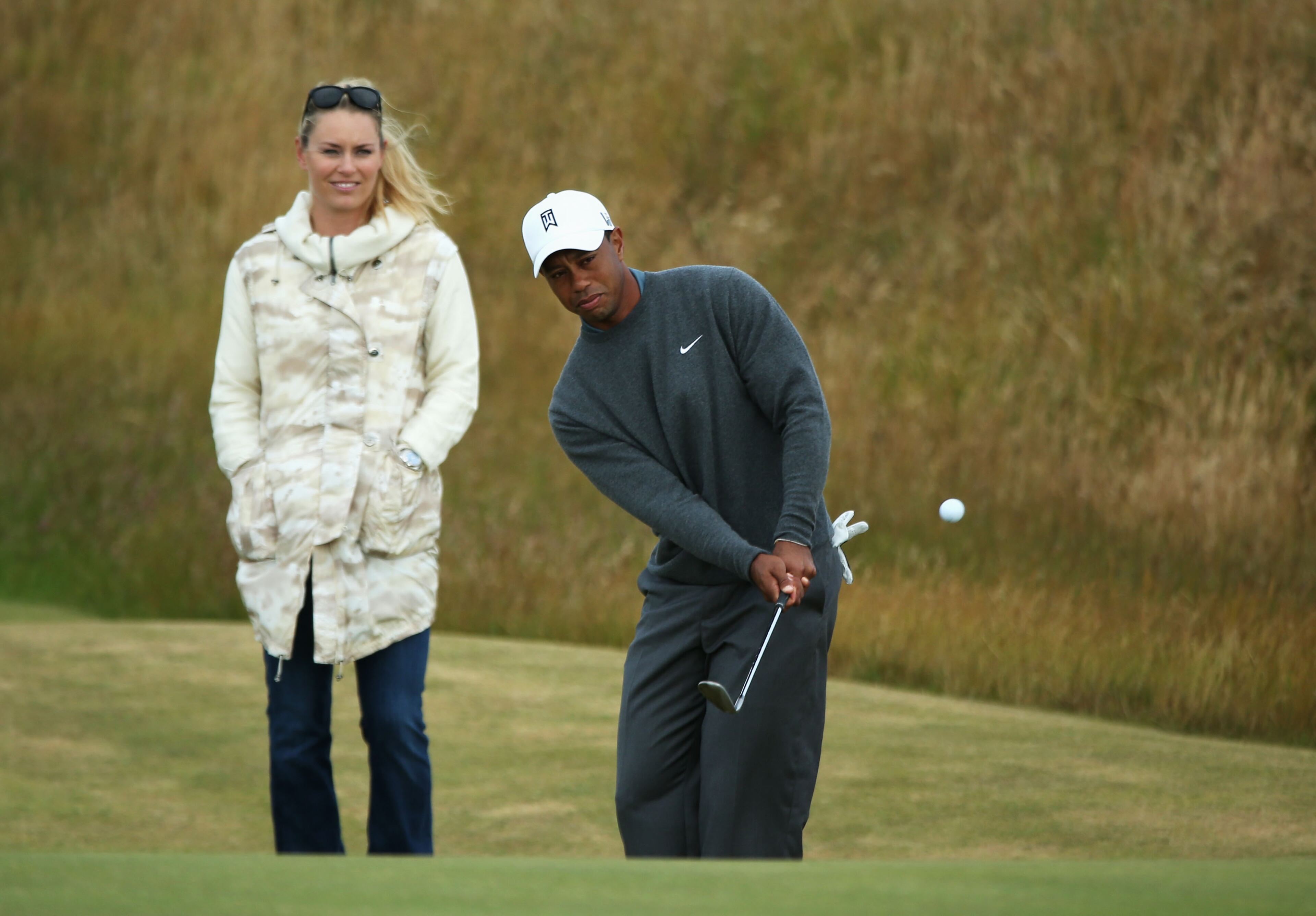 Tiger Woods of the United States chips the ball while skier Lindsey Vonn watches ahead of the 142nd Open Championship at Muirfield on July 15, 2013 in Gullane, Scotland. (Photo by Andy Lyons/Getty Images)
