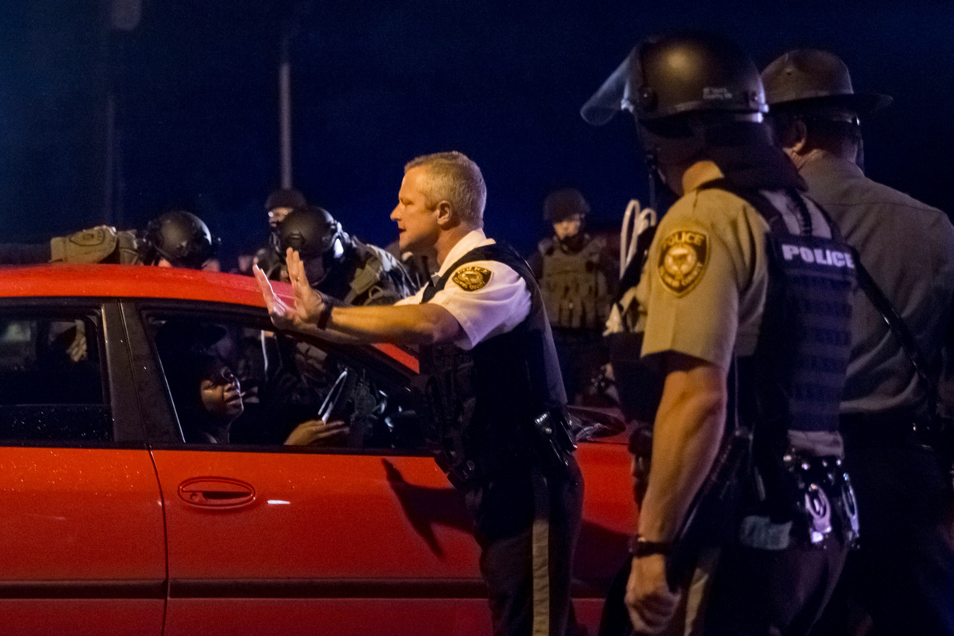 Police officers attempt to move a vehicle back after shots were fired on West Florissant Avenue on the anniversary of Michael Brown's death in Ferguson, Mo., Aug. 9, 2015. A day of peaceful protest commemorating the killing of an unarmed black teenager by a white police officer one year ago ended in gunfire late Sunday. A St. Louis County police officer was involved in the shooting, the department said. (Whitney Curtis/The New York Times)
