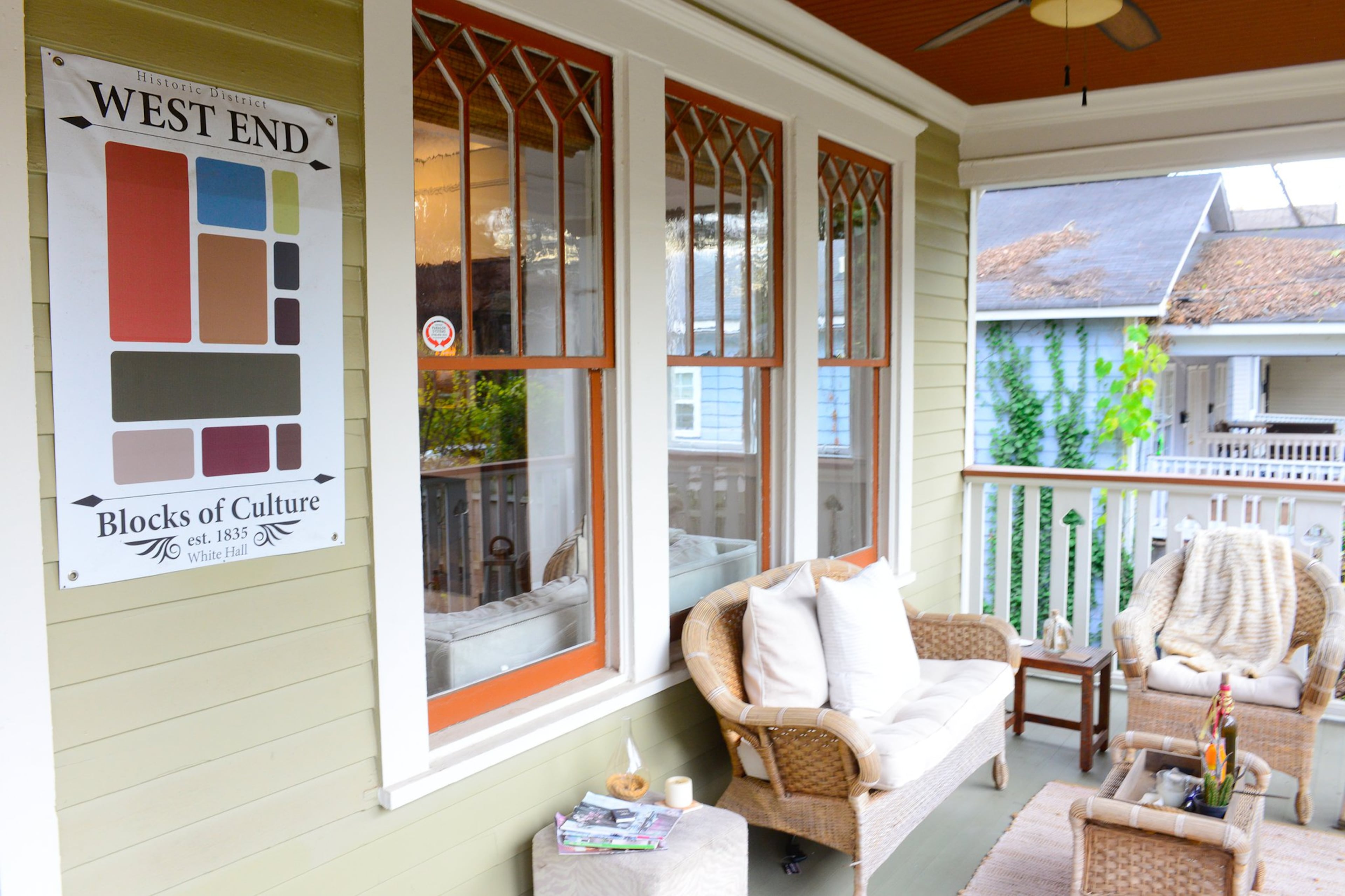 The front porch of Corey and Joy Jones' home features traditional Craftsman windows with orange trim and is bordered by white railings with unique arrow-shaped cutouts. The porch is decorated with furniture from secondhand stores and new pillows and seat cushions from Pier 1 Imports and HomeGoods.