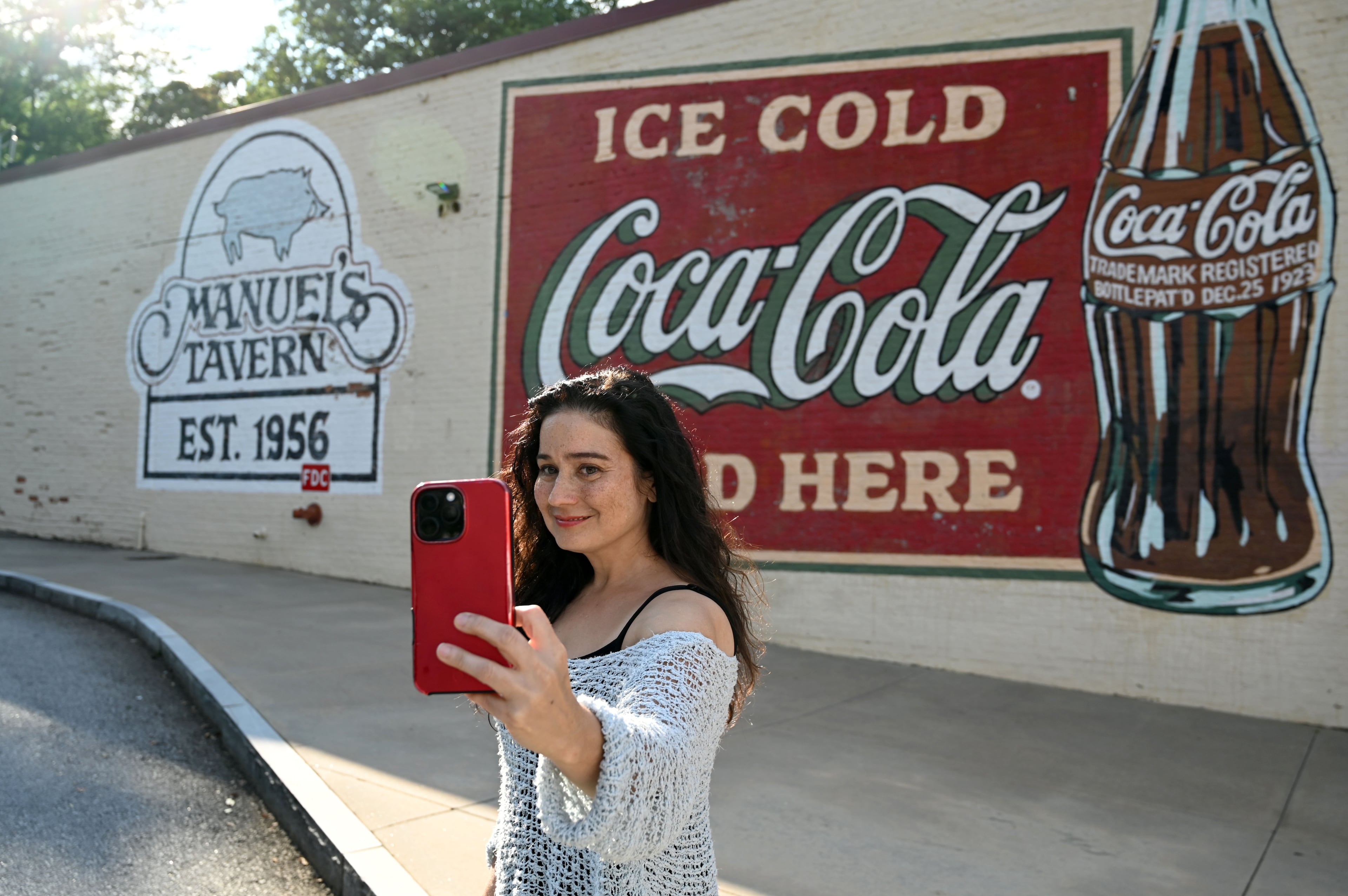 Shannon Byrne takes a selfie in front of the Manuel’s Tavern sign on Thursday, Aug. 6, 2026, in Atlanta. (Hyosub Shin/AJC)