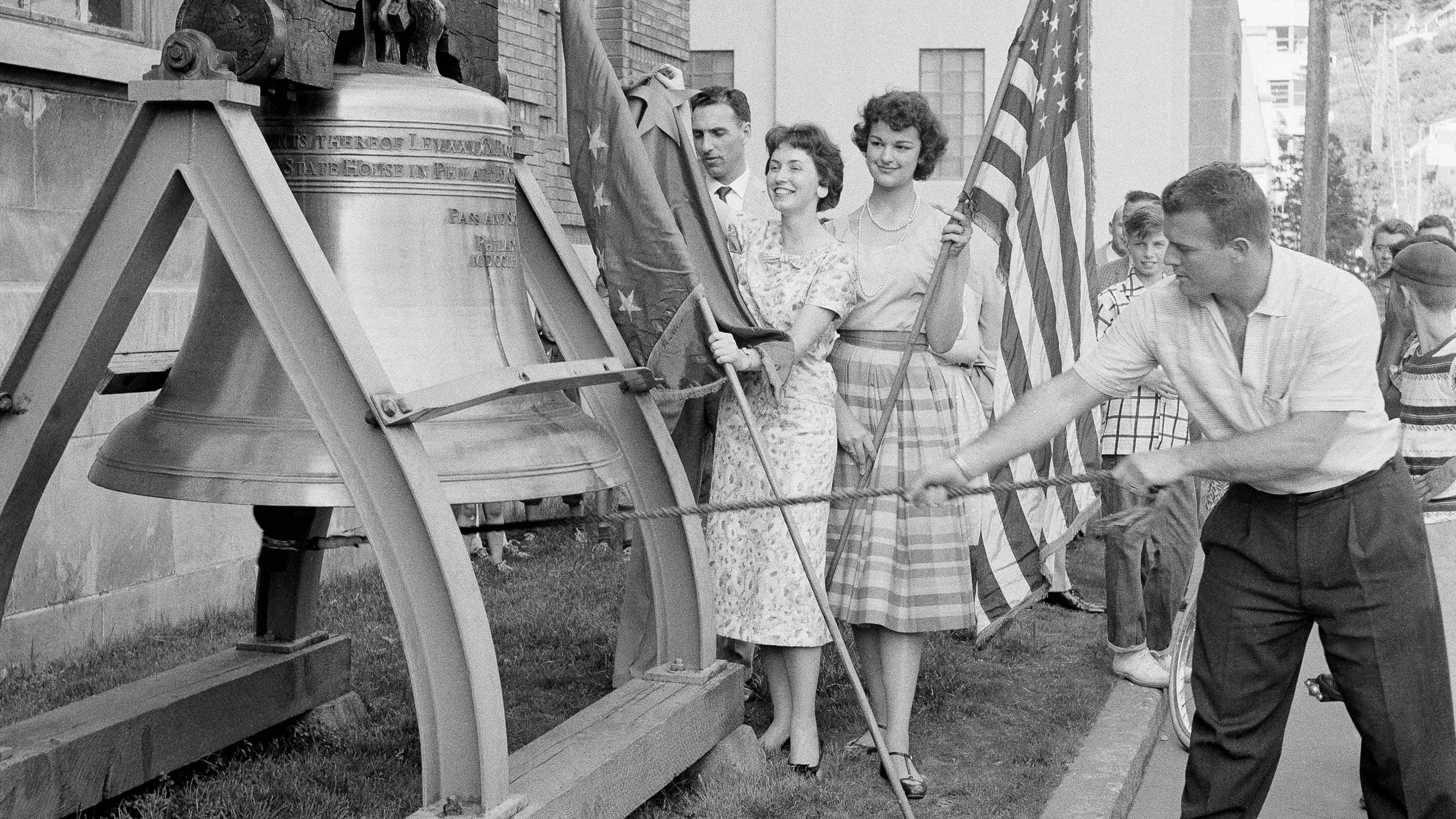FILE - Romer Derr rings a replica of the Liberty Bell outside the Federal Building 49 times, signifying Alaska's joining the United States as the 49th state, on July 1, 1958, in Juneau, Alaska. Behind Derr holding the Alaska flag, left, is Judy Findlay and holding the U.S. flag, right, is Marilee Nowacki. (AP Photo/JK, File)