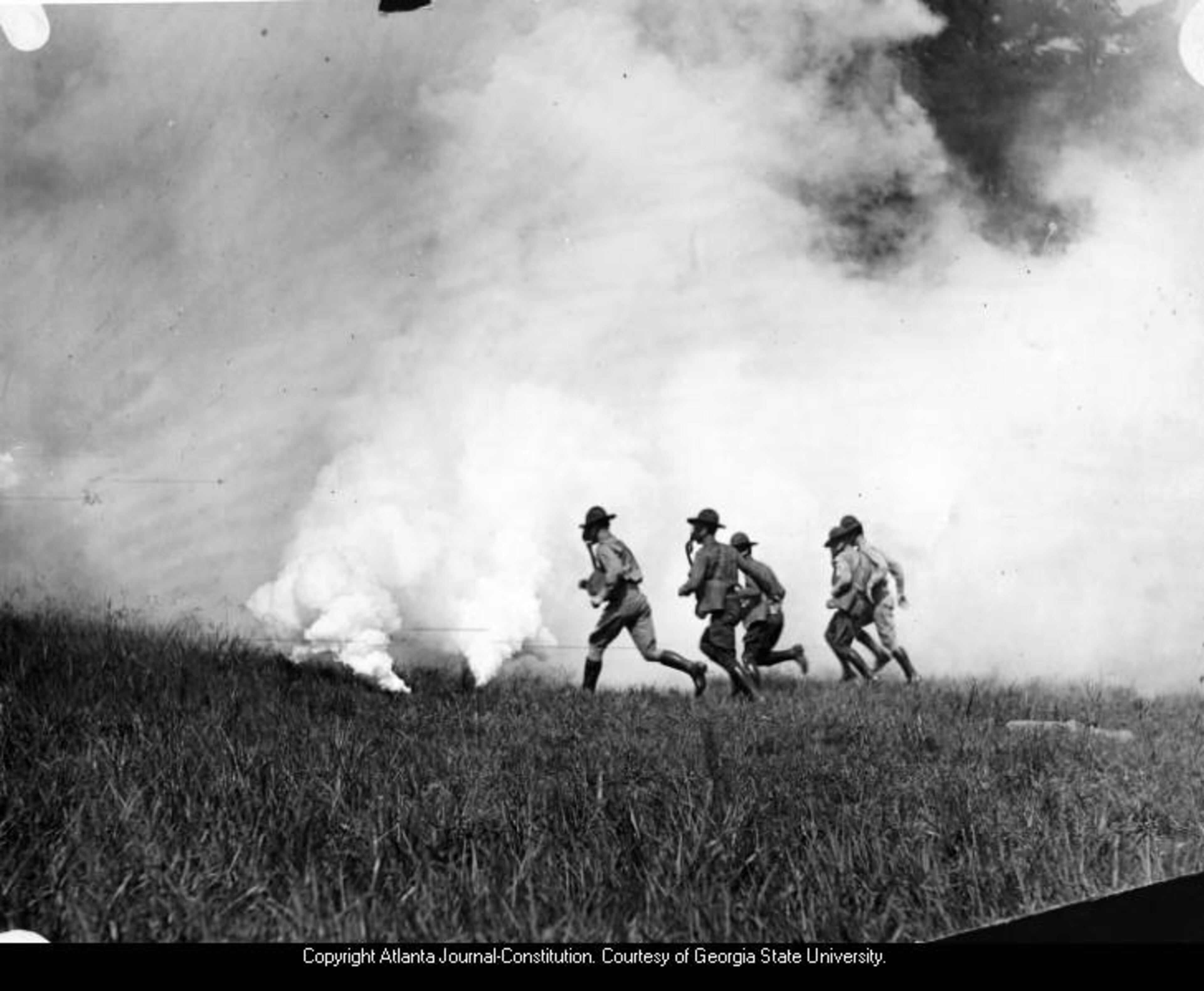 Circa 1910s-20s -- Four soldiers on training exercise, wearing gas masks, run through a field with smoke-bombs at Fort Benning. AJC PHOTO ARCHIVES