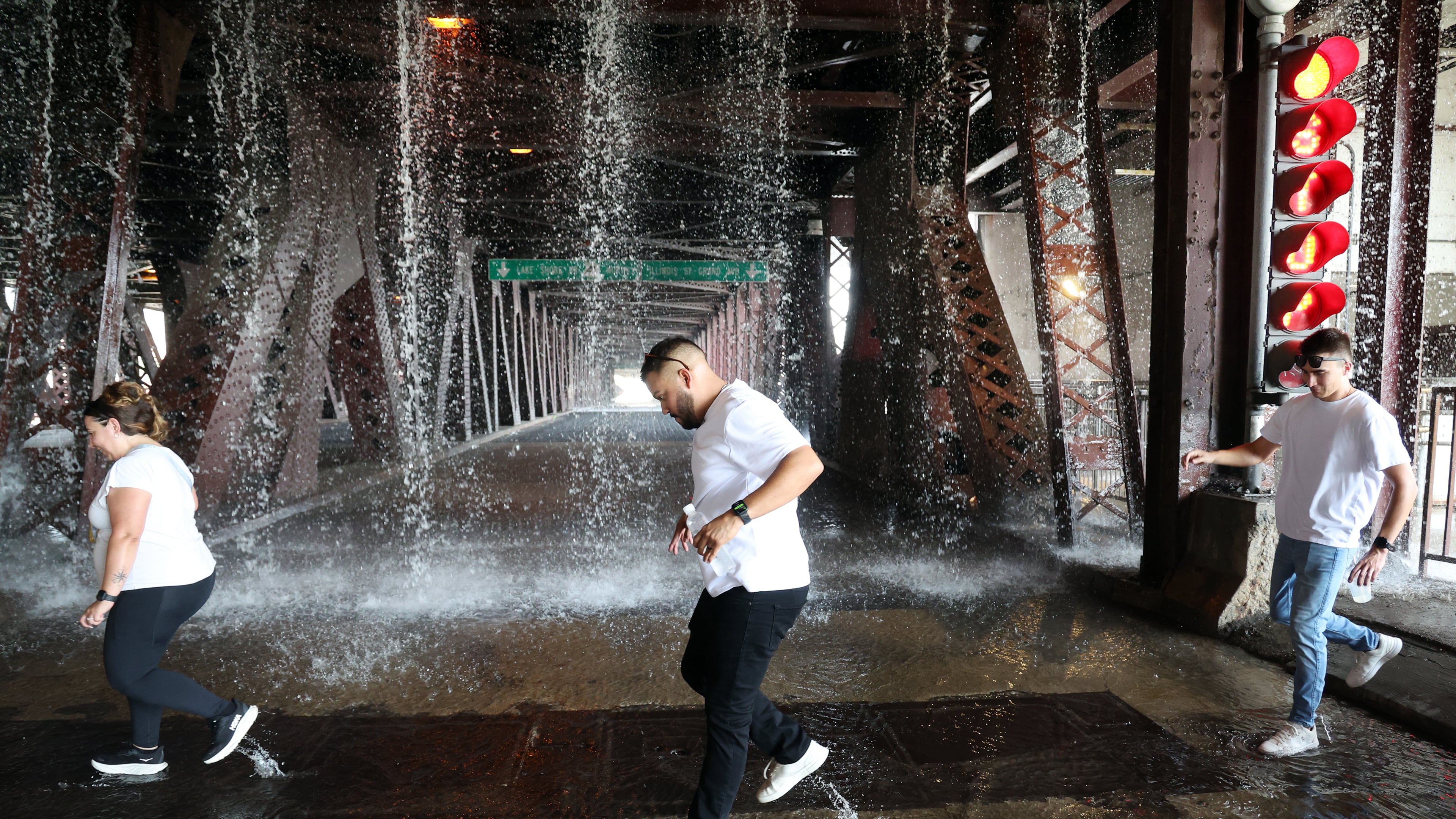 People scamper west across the lower level of the DuSable Lake Shore Drive bridge over the Chicago River on Wednesday, Sept. 2, 2026, as water pumped by a Chicago Fire Department boat flows down onto the double-leaf, double-deck, fixed counterweight bridge. (Terrence Antonio James/Chicago Tribune via AP)