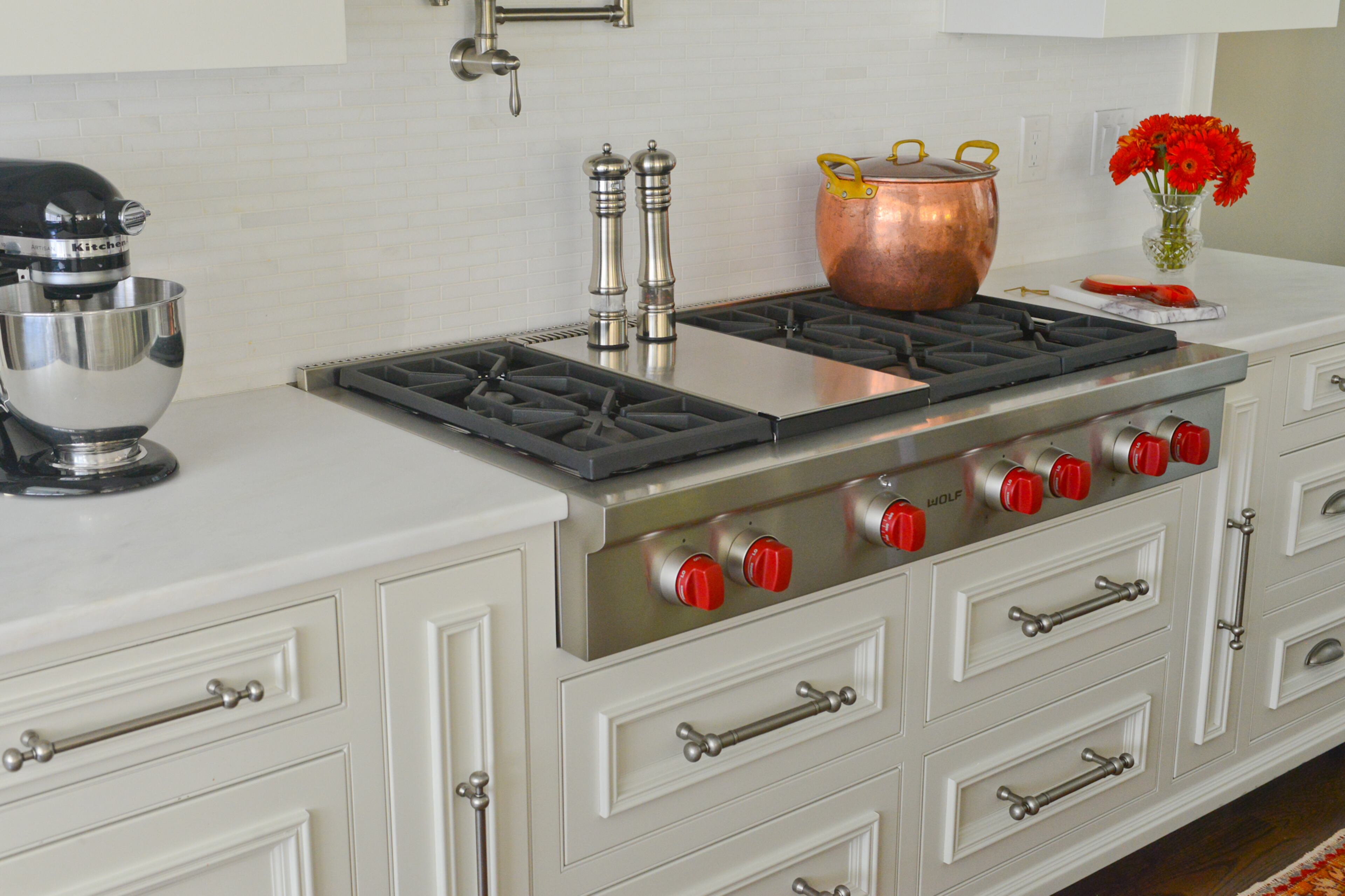 Red knobs on a Wolf cooktop provide punch of color in the white kitchen.