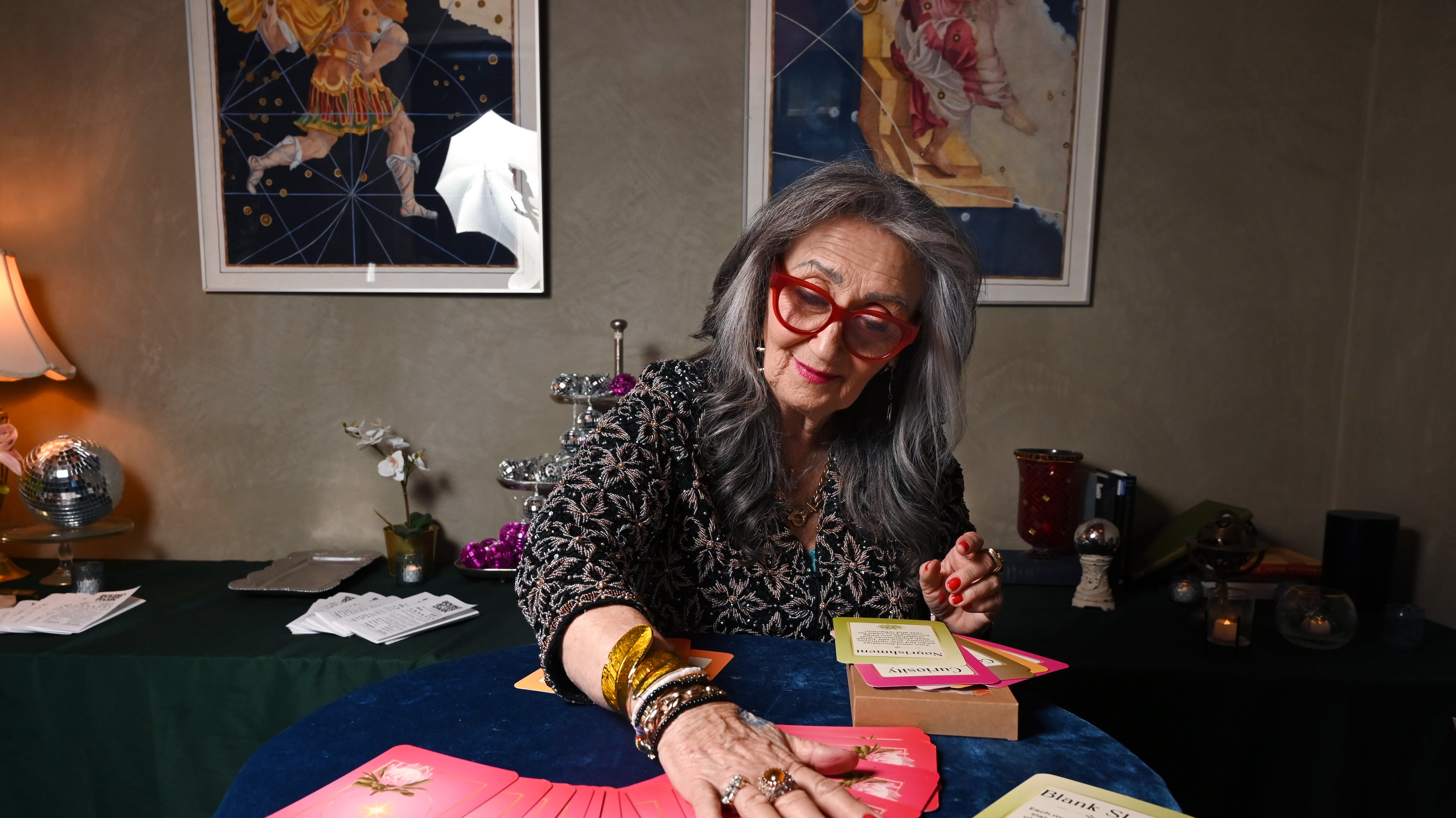 Healing practitioner Rolene Jaffe shows Rise & Radiate oracle cards, which Jaffe created, at 7th House, an astrological-themed restaurant where her son, Alexander Sher, is part owner, on Wednesday, April 1, 2026, in Atlanta. (Hyosub Shin/AJC)