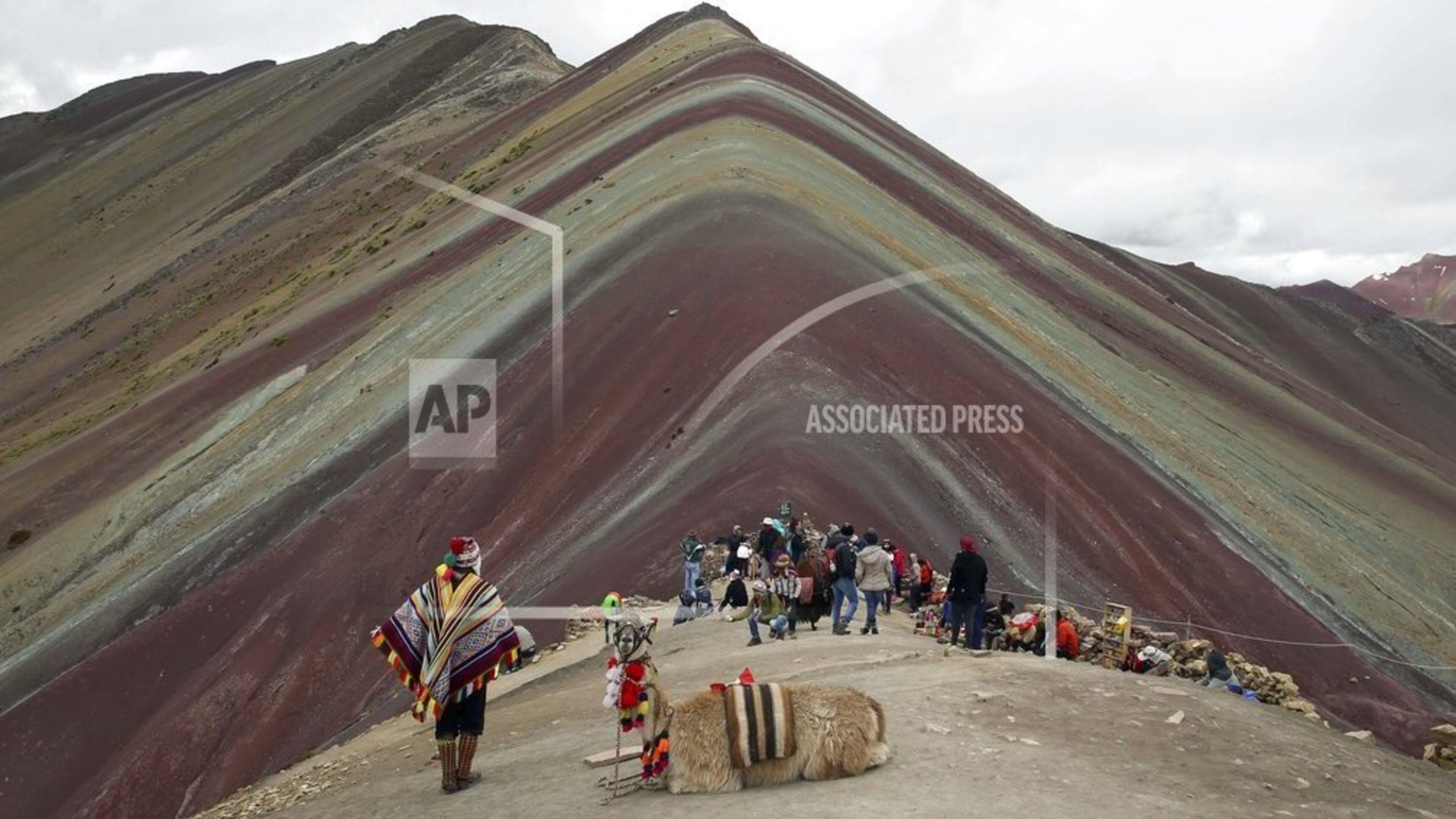 In this March 2, 2018 photo, an Andean man rests with his llama on Rainbow Mountain in Pitumarca, Peru. Tourists gasp for breath as they climb for two hours to the 16,404-foot (5,000-meter) peak in the Peruvian Andes, but stunned by the magical beauty that unfurls before them. (AP Photo/Martin Mejia)