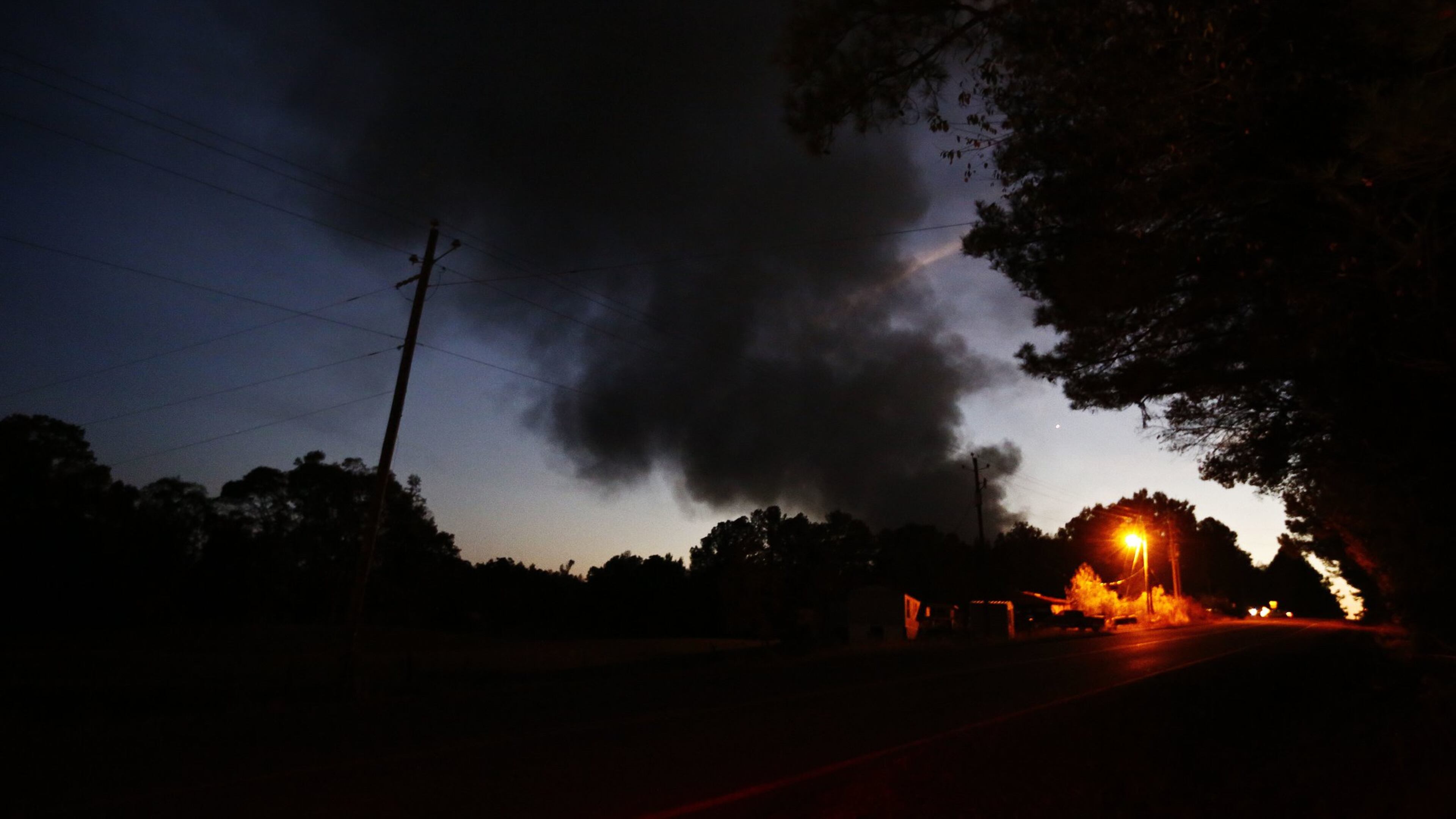 Light from a light pole shows a house near a plume of smoke from a Colonial Pipeline explosion Monday in Helena, Ala. Colonial said in a statement that a damaged gasoline pipeline will remain closed this week but a second line carrying other fuels has reopened. One worker was killed and several were injured. (AP Photo/Brynn Anderson)