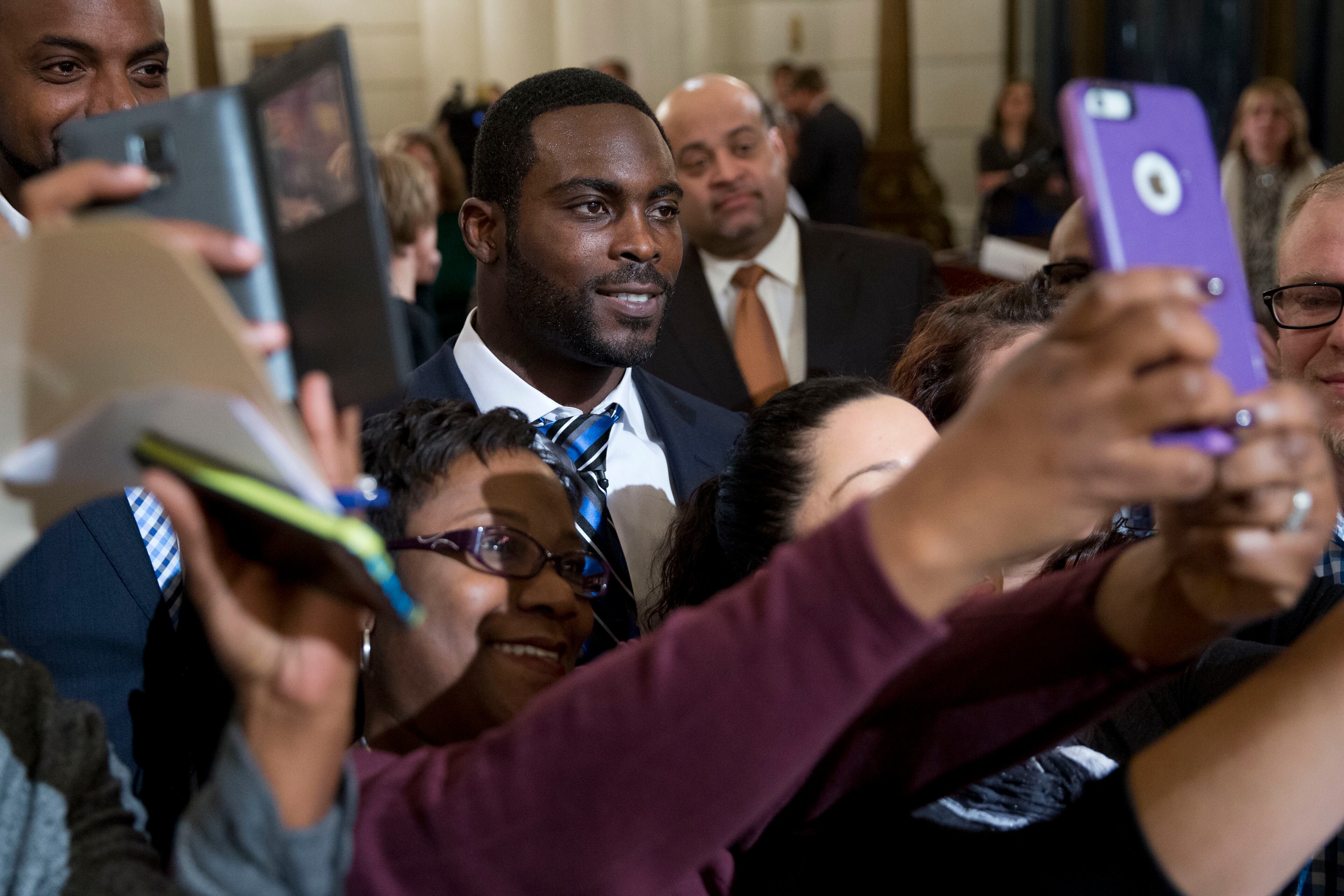 Pittsburgh Steelers quarterback Mike Vick poses for selfies after a news conference Tuesday, Dec. 8, 2015, at the state Capitol in Harrisburg, Pa. Vick is lobbying Pennsylvania legislators on a bill that would help protect pets left in hot cars. Vick was a star quarterback for the NFL's Atlanta Falcons when he pleaded guilty in 2007 to being part of a dogfighting ring and ended up serving 21 months in prison. (AP Photo/Matt Rourke)