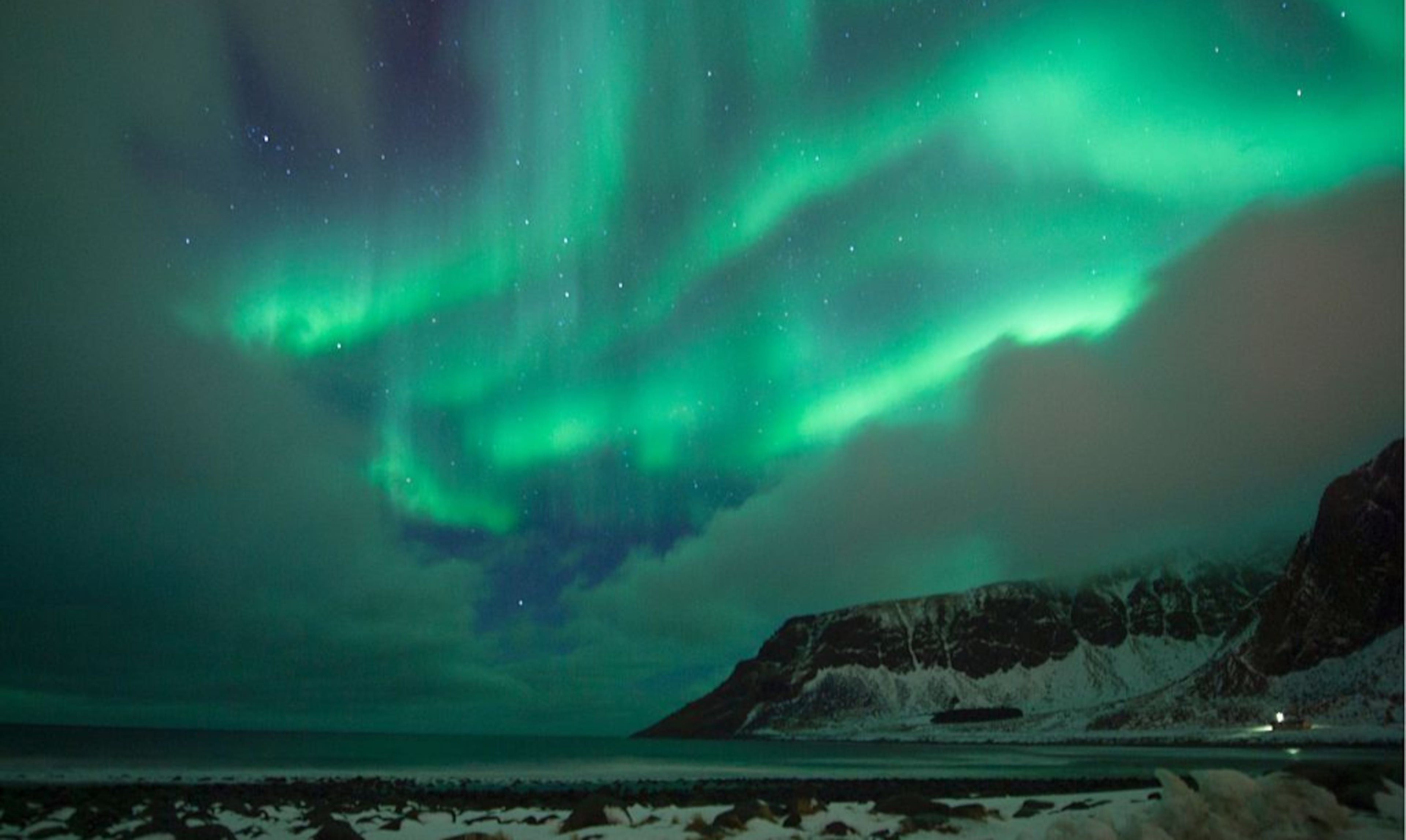Northern lights ( aurora borealis ) illuminated the sky over a snow covered beach in the Arctic Circle in March of 2016.