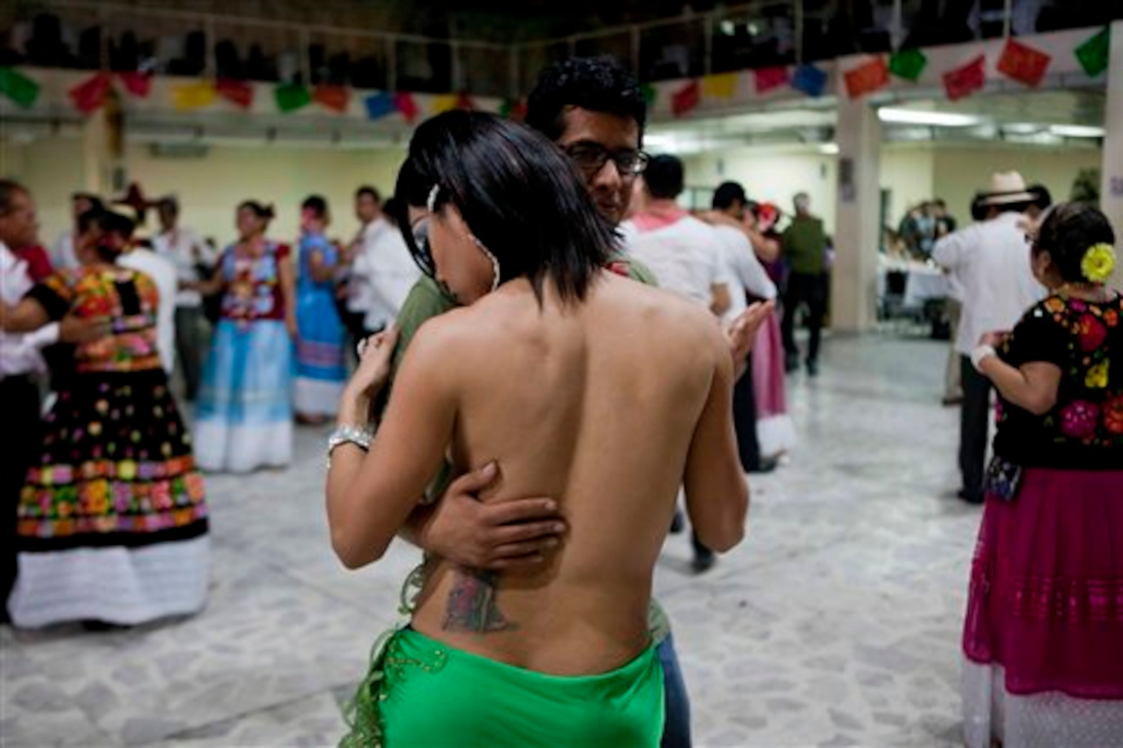 In this June 29, 2013 photo, a Zapotec indigenous man who dresses and behaves in ways associated with women known as a muxe, back to camera, dances with a man at a party in Mexico City. A group of Muxes, (pronounced MOO-shays), living in Mexico City gathered to share their traditions at a community party or "vela," as the event is called in their hometown Juchitan, a city of Zapotecs in the southern state of Oaxaca. Gay men, transvestites and transgender people are generally accepted in Juchitan and often work as home helpers, embroiderers, decorators, cooks and entertainers. (AP Photo/Eduardo Verdugo)
