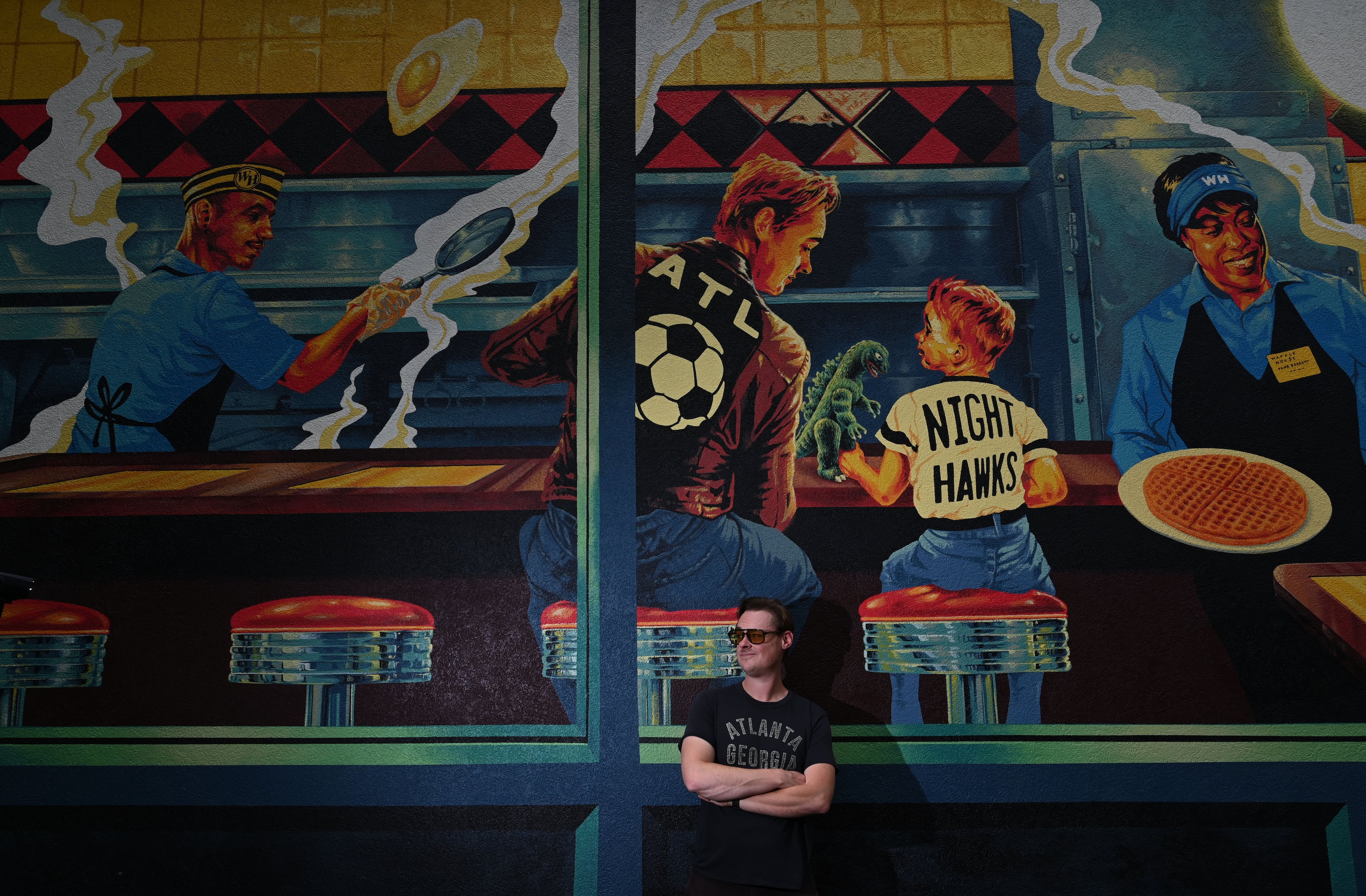 Artist Nick Benson poses for a portrait in front of his mural. He included a self portrait of himself in the style of Norman Rockwell's iconic painting, "The Runaway." (Hyosub Shin/AJC)