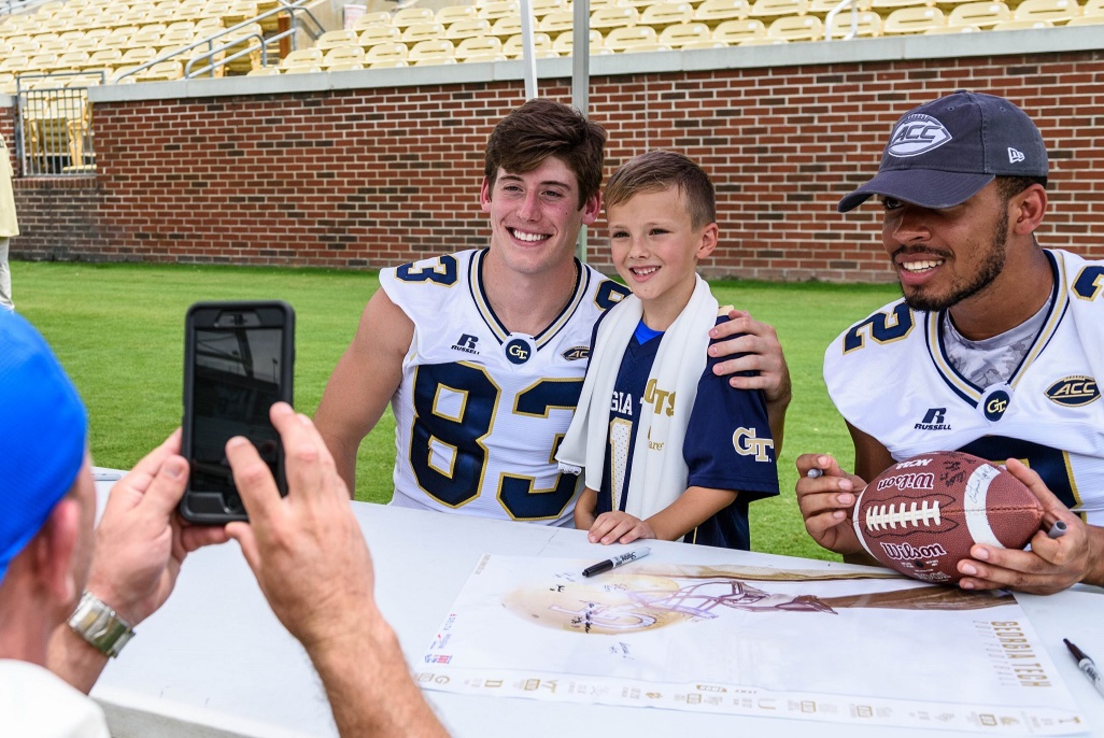 Georgia Tech wide receivers Brad Stewart (83) and Ricky Jeune (2) pose for a photo with a fan during Fan Day at Bobby Dodd Stadium on Aug. 12, 2017. -- Danny Karnik/GT Athletics