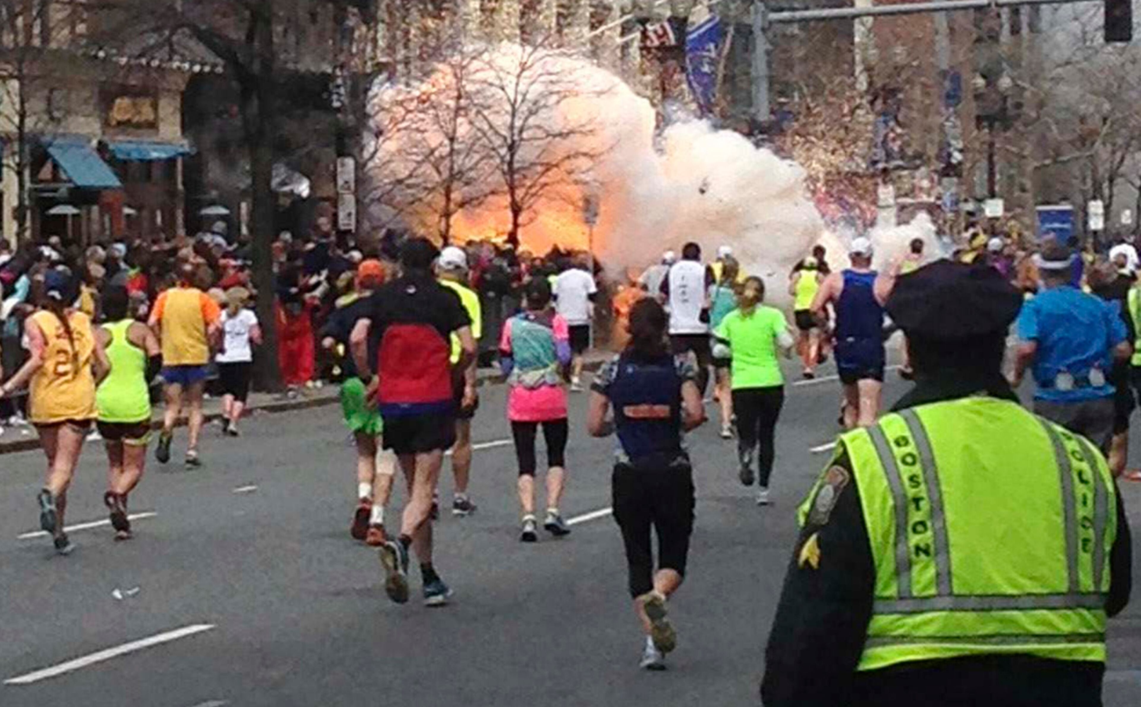Runners continue to run towards the finish line of the Boston Marathon as an explosion erupts near the finish line of the race. Two simultaneous explosions ripped through the crowd at the finish line of the Boston Marathon, killing at least two people and injuring dozens on a day when tens of thousands of people pack the streets to watch the world famous race.