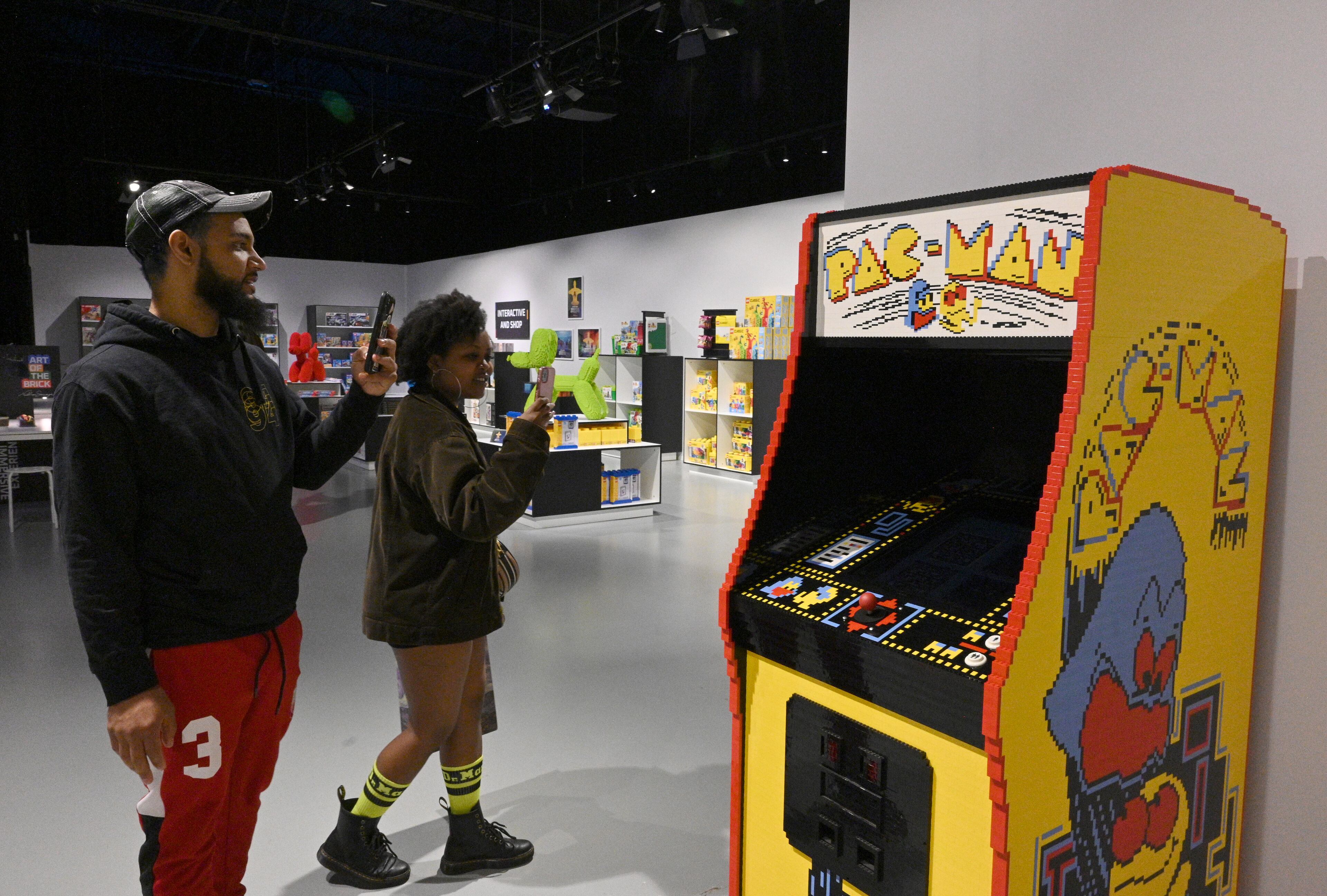 Moe Lee (left) and Evelyne Gichingiri take pictures of Pac-Man game machine made with Lego bricks at Exhibition Hub Atlanta Art Centre, Wednesday, April 19, 2023, in Doraville. The exhibition will feature many pieces and themes, including a room with oversized sculptures (25-foot long), over 70 works of art crafted from more than 1 million LEGO bricks, galleries celebrating human-kind and nature, and a short documentary about how Nathan creates his works. (Hyosub Shin / Hyosub.Shin@ajc.com)