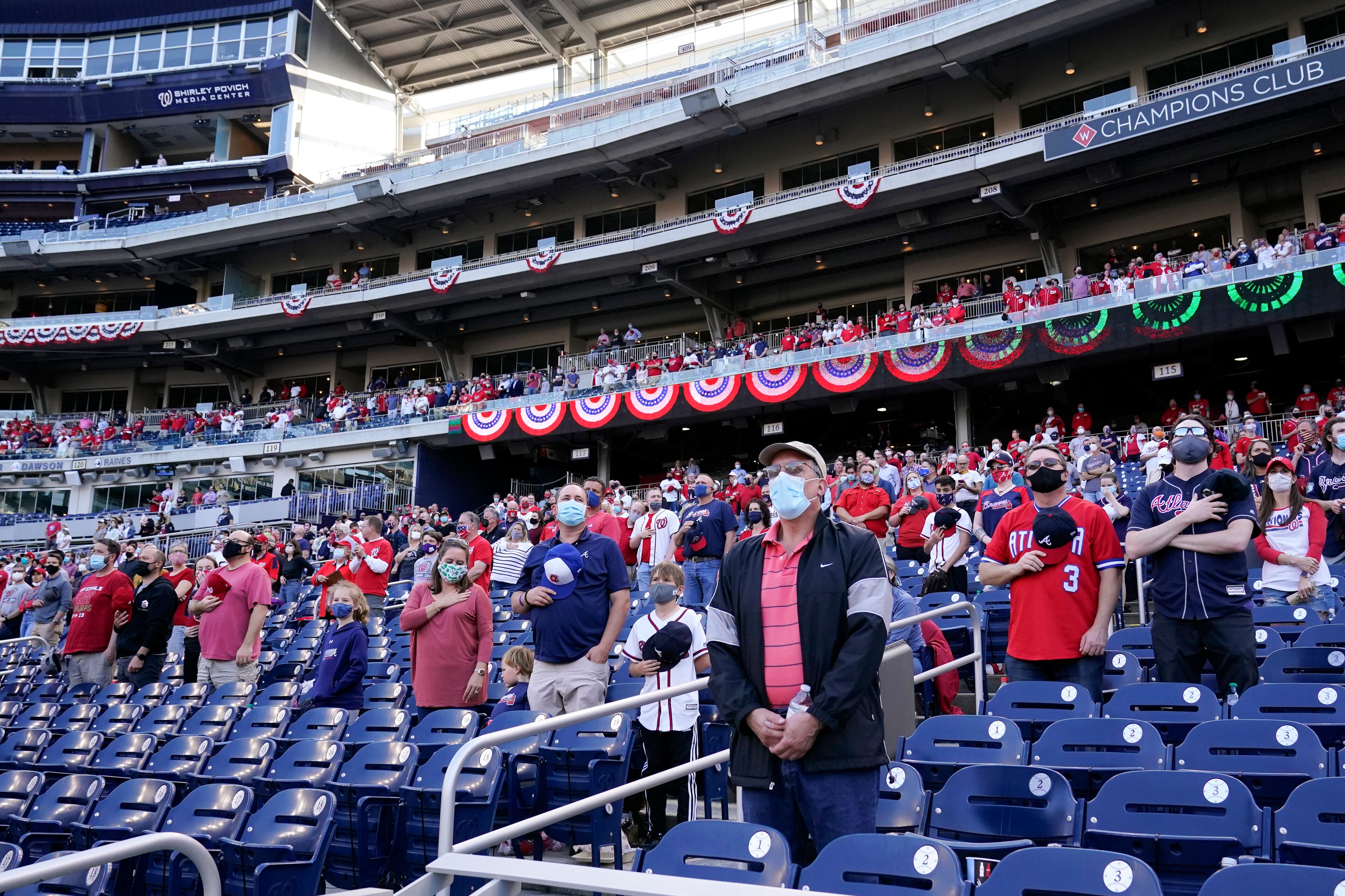 Fans stand socially distanced during a rendition of "God Bless America" during the seventh inning stretch of an opening day baseball game between the Atlanta Braves and the Washington Nationals at Nationals Park, Tuesday, April 6, 2021, in Washington. (AP Photo/Alex Brandon)