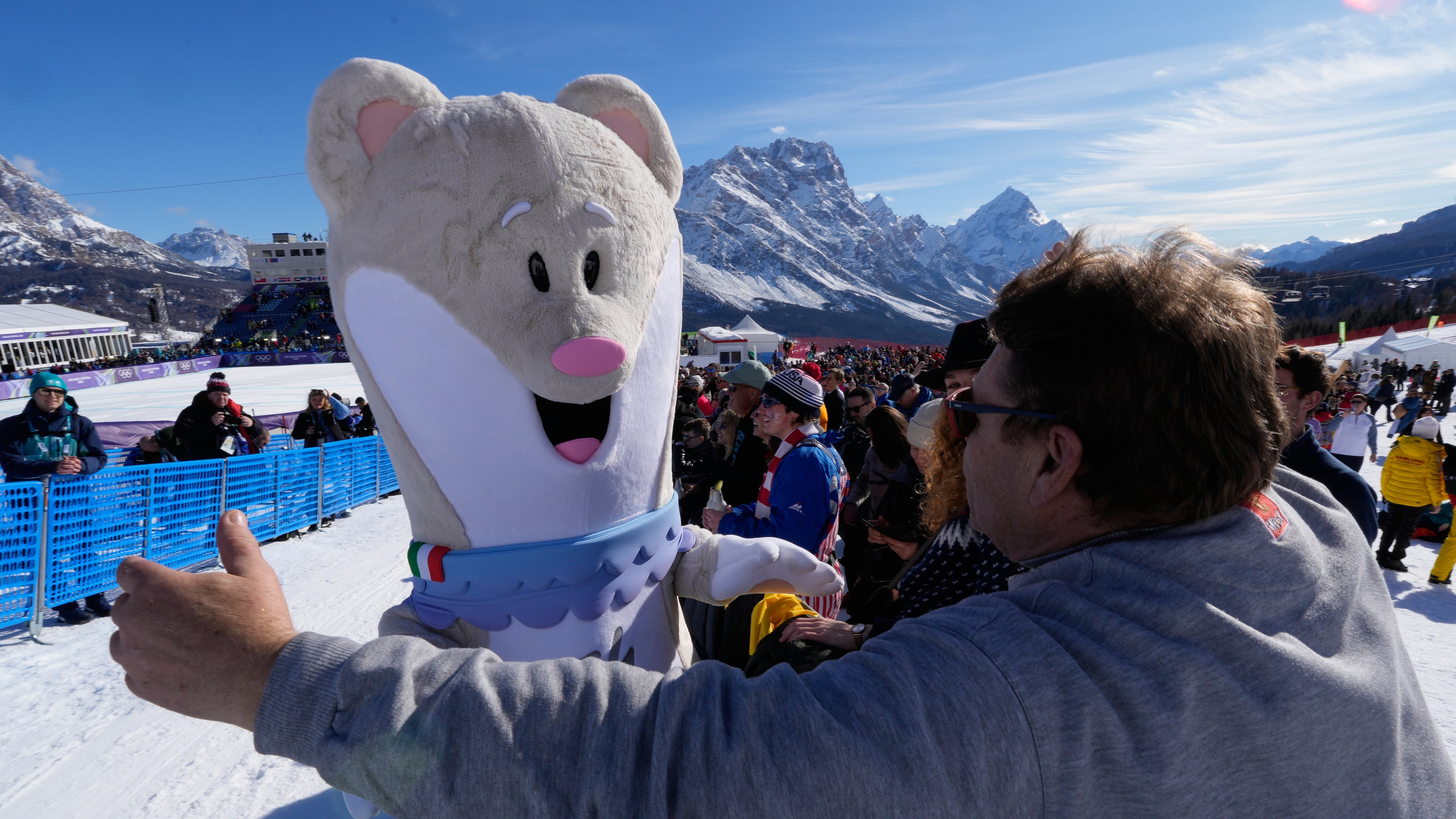 A spectator moves in to hug Olympic mascot Tina prior to an alpine ski women's downhill race, at the 2026 Winter Olympics, in Cortina d'Ampezzo, Italy, Sunday, Feb. 8, 2026.. (AP Photo/Robert F. Bukaty)