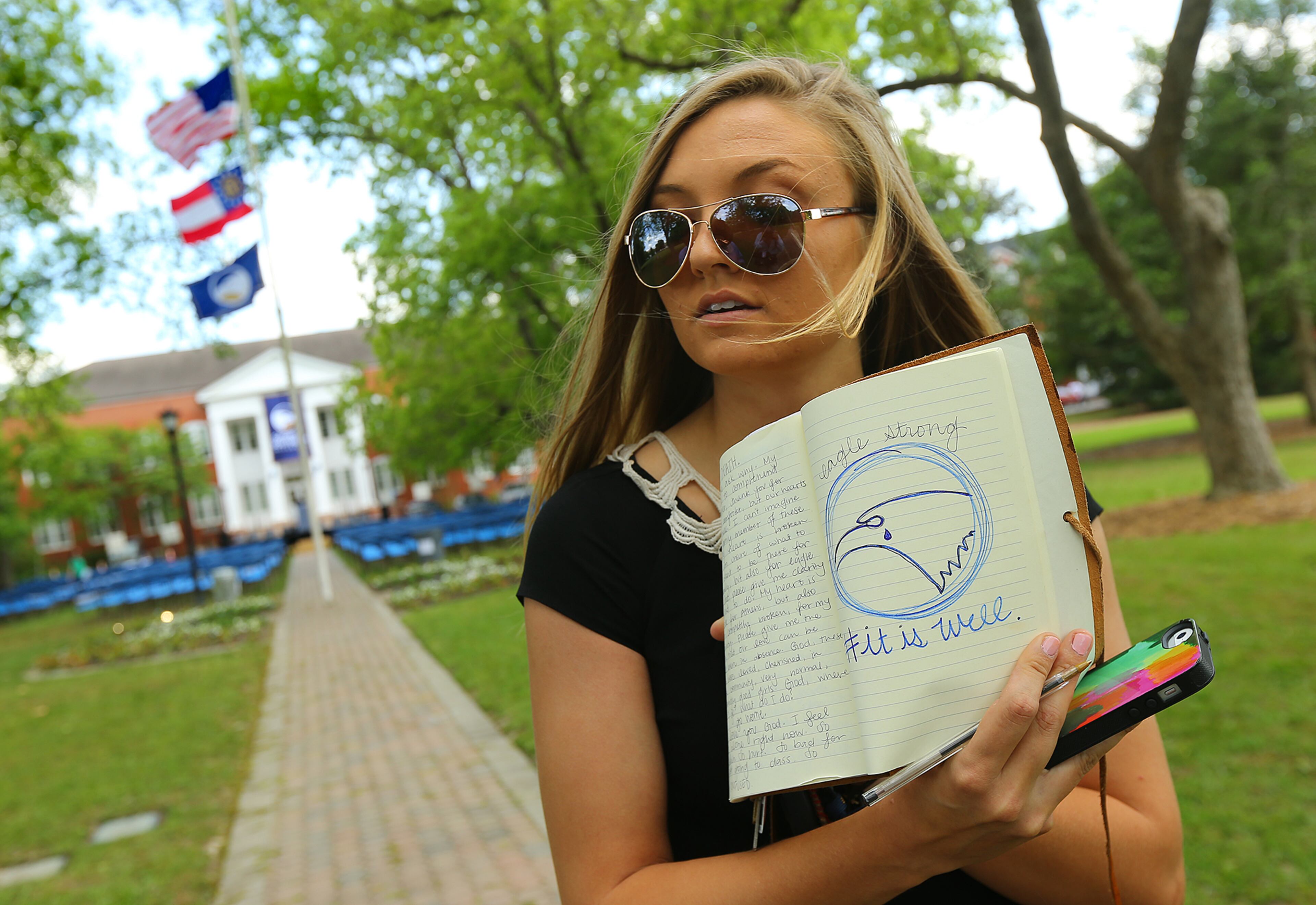 The flags fly at half-staff at Georgia Southern University while senior Katie Pursley, 21, visits the Memorial Service site on Sweetheart Circle for those students whose lives were tragically lost on Thursday, April 23, 2015, in Statesboro. Pursley, from Athens, keeps a daily journal in which she drew the school mascot, an eagle, with a tear to symbolize the grief of the university. Curtis Compton / ccompton@ajc.com