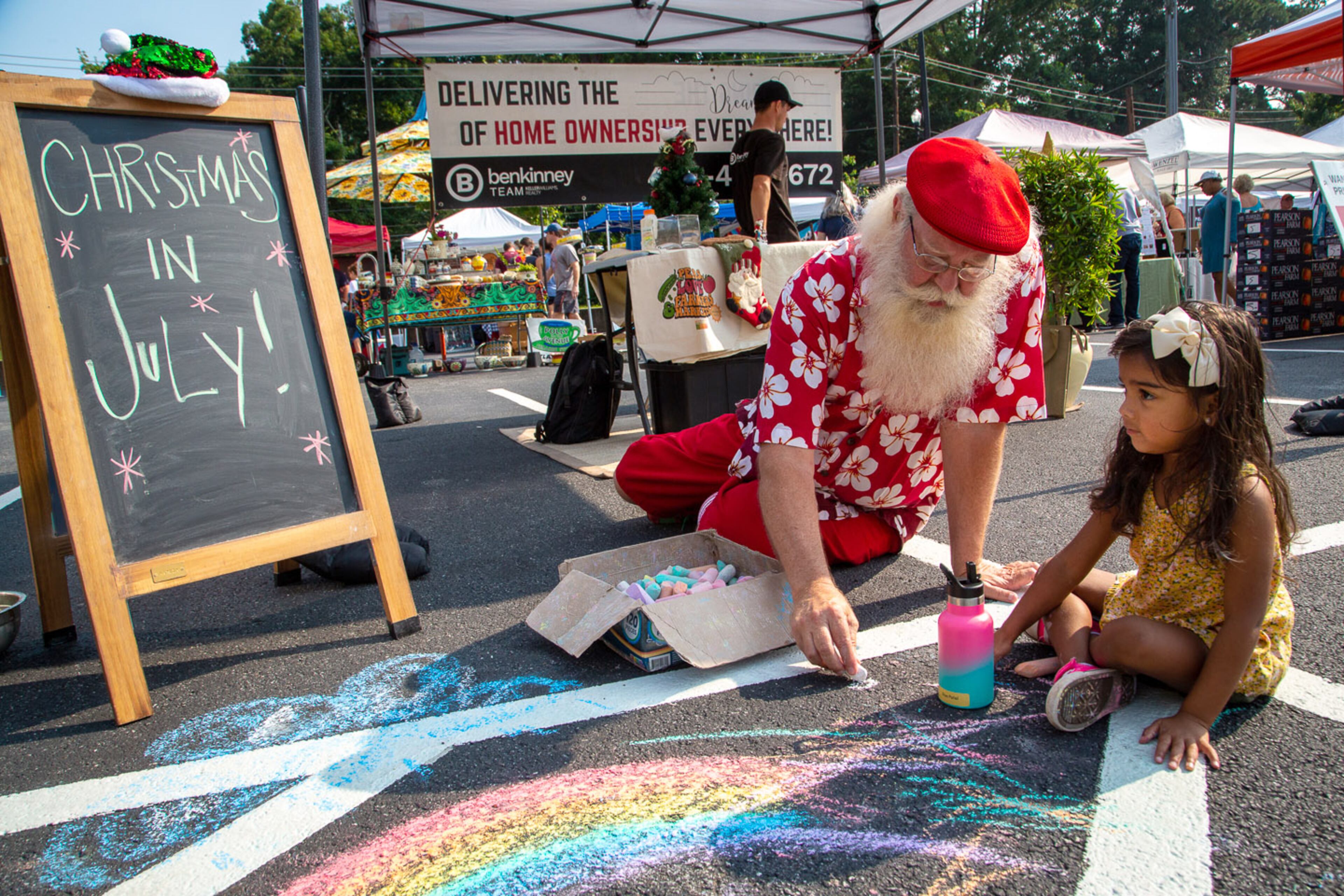 Santa Glenn Johnson and Siya Patel draw on the sidewalk during the Christmas in July celebration at the Brookhaven Farmers Market on Saturday, July 24, 2021. (Photo: Steve Schaefer for The Atlanta Journal-Constitution)