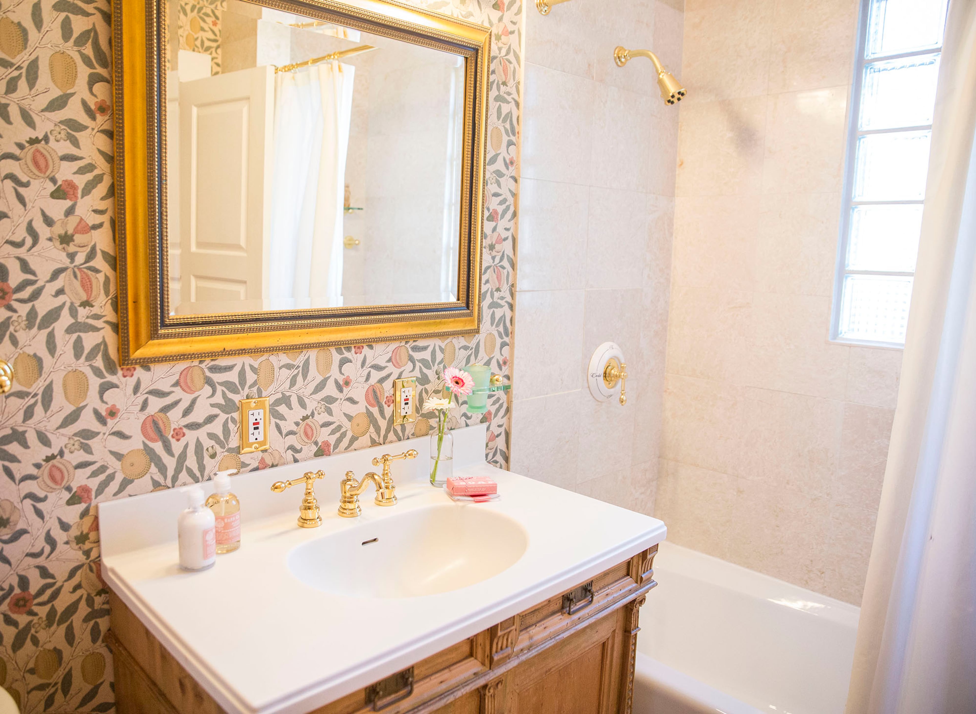 The guest bath incorporates an antique Danish table repurposed as a vanity and finished with Kohler fixtures. Morris & Co.'s Pomegranate wallpaper adds a touch of whimsy.