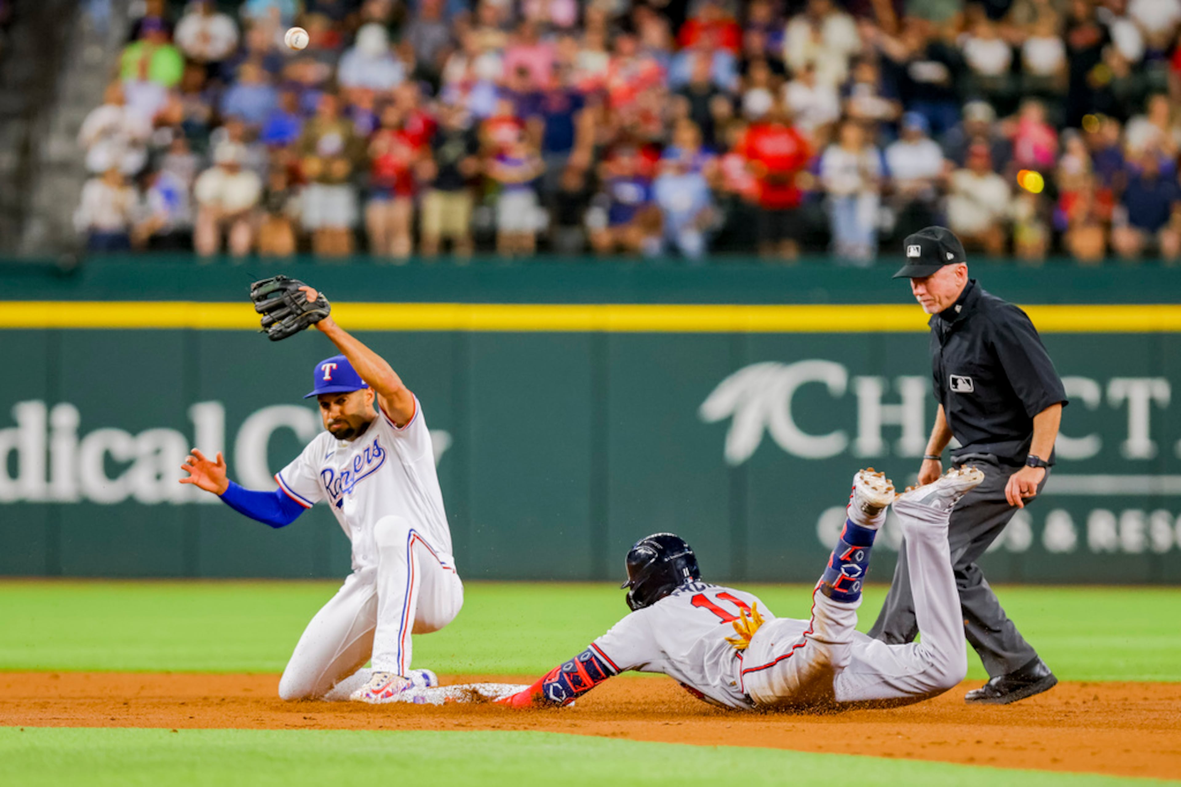 Atlanta Braves' Orlando Arcia, center, slides into second base after hitting a double while Texas Rangers second baseman Marcus Semien, left, attempts to field the ball in the top of the second inning of a baseball game in Arlington, Texas, Monday, May 15, 2023. (AP Photo/Gareth Patterson)