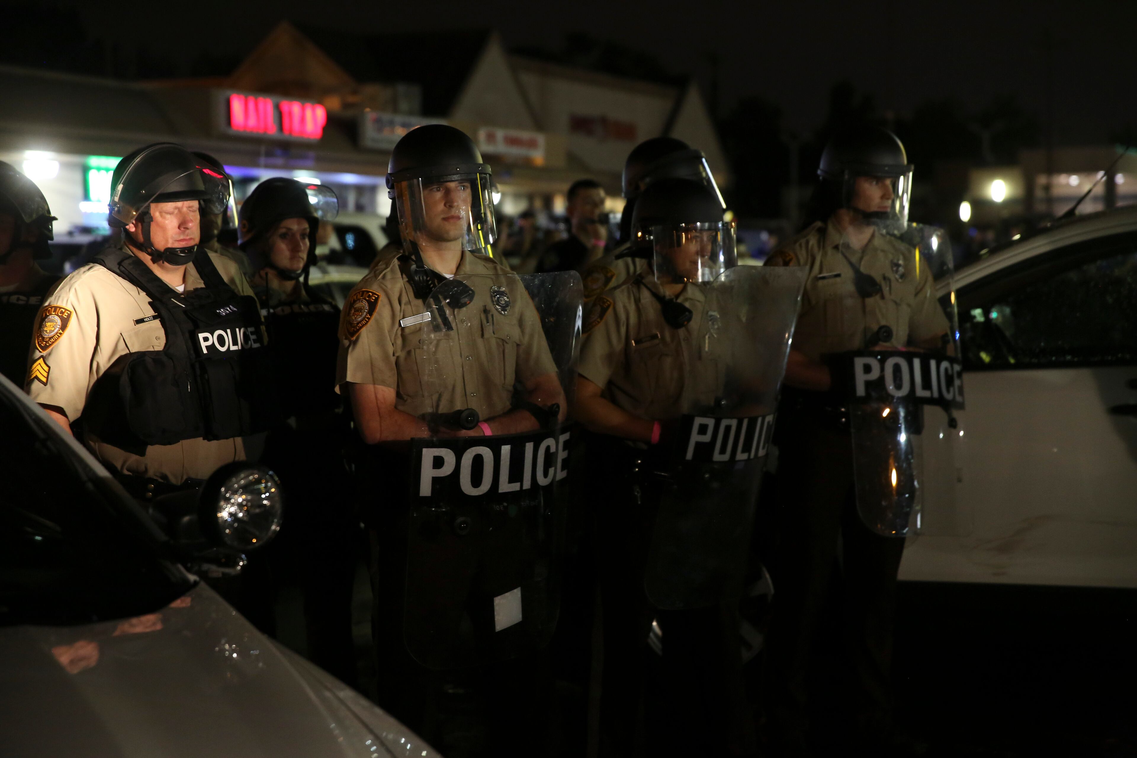 Police officers in riot gear gather on West Florissant Avenue as protesters march on the anniversary of the fatal shooting of Michael Brown by a police officer in Ferguson, Mo., Aug. 9, 2015. A day of peaceful protest commemorating the killing of an unarmed black teenager by a white police officer one year ago ended in gunfire later Sunday. A St. Louis County police officer was involved in the shooting, the department said. (Whitney Curtis/The New York Times)