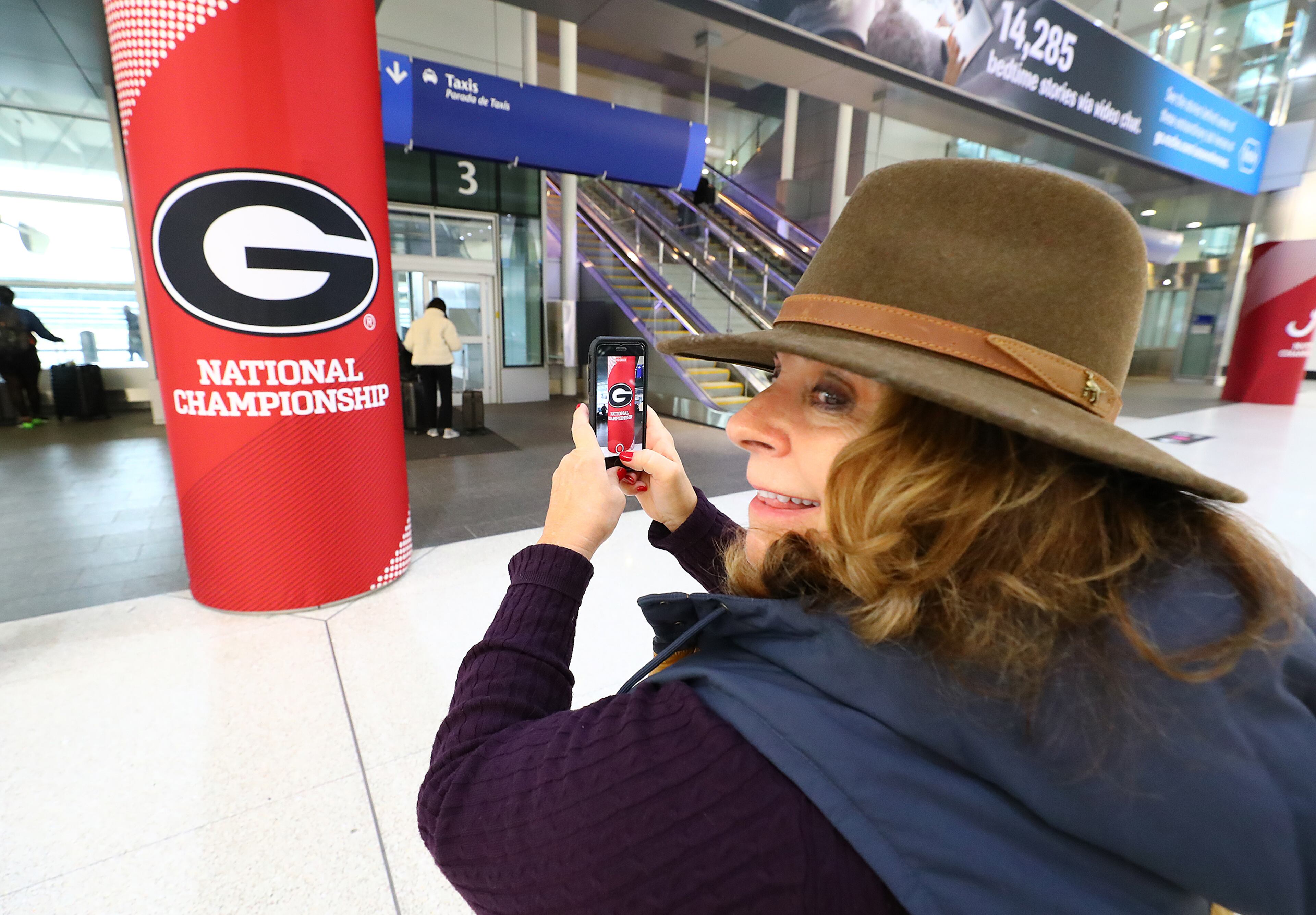 010622 Indianapolis: Georgia fan Carol Monroe snaps a photo of the Georgia National Championship sign as she arrives for the big game at the Indianopolis International Airport on Thursday, Jan. 6, 2022, in Indianapolis. “Curtis Compton / Curtis.Compton@ajc.com”`