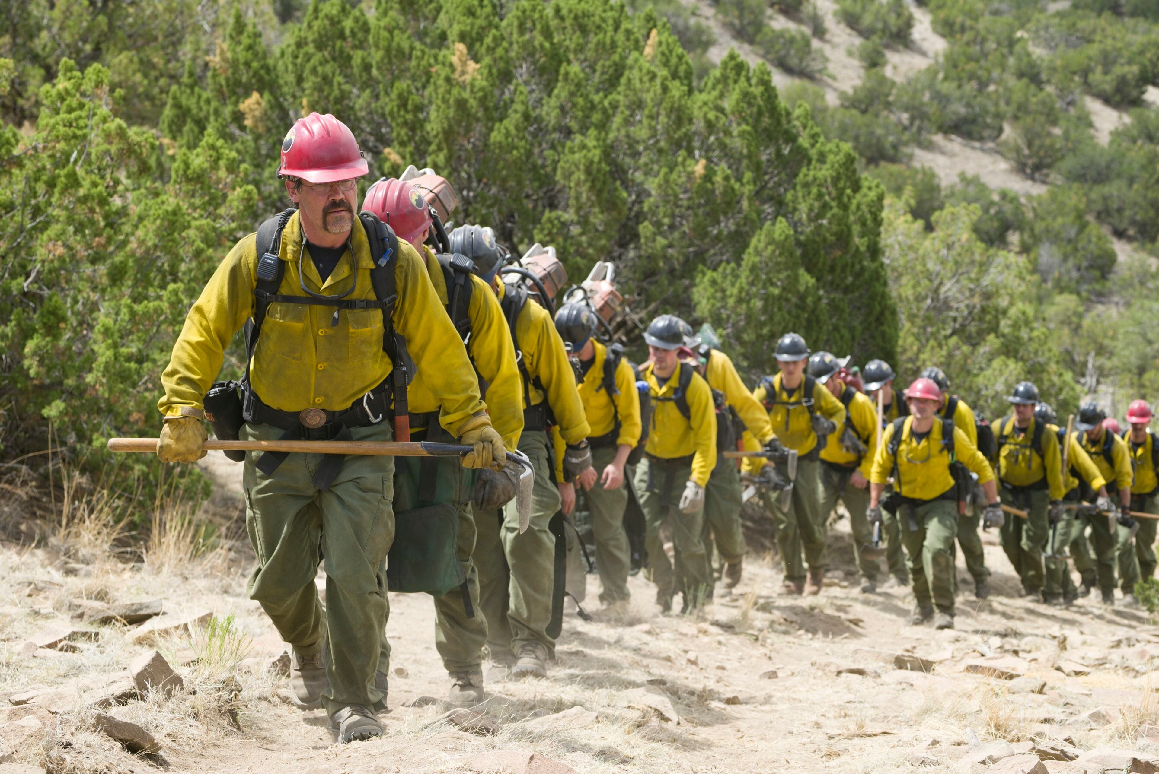 "Supe" Eric Marsh, played by Josh Brolin, leads the Granite Mountain Hotshots up the trail at Yarnell Hills--including, generally in this order: Travis Carter (Scott Foxx), Dustin Deford (Ryan Busch), Garret Zuppiger (Brandon Bunch), Andrew Ashcraft (Alex Russell), Wade Parker (Ben Hardy), Scott Norris (producer Thad Luckinbill), Anthony Rose (Jake Picking), Travis Turbyfill (Geoff Stults), Chris MacKenzie (Taylor Kitsch), Brendan McDonough (Miles Teller), Joe Thurston (Matthew Van Wettering), Kevin Woyjeck (Michael McNulty), Grant McKee (Sam Quinn), Billy Warneke (Ryan Jason Cook), John Percin, Jr. (Nicholas Jenks), Sean Misner (Kenny Miller), Robert Caldwell (Dylan Kenin), Clayton Whitted (Scott Haze), Jesse Steed (James Badge Dale) in Columbia Pictures' the Brave."