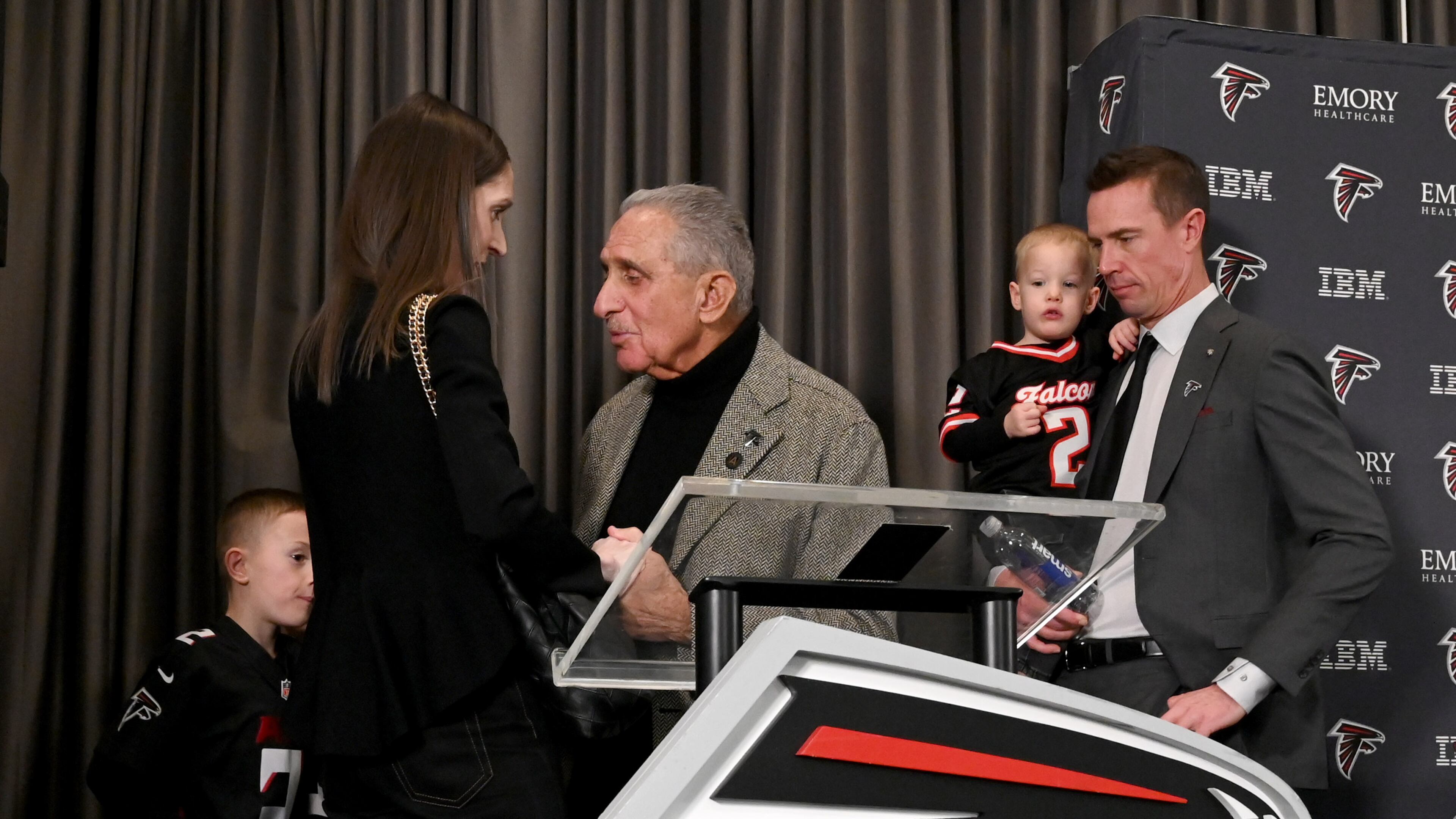 Atlanta Falcons owner Arthur M. Blank (center) holds the hand of Sarah Ryan, wife of Matt Ryan (right), as the new Atlanta Falcons president of football holds his son, Cal, after a news conference Tuesday, Jan. 13, 2026, in Flowery Branch. (Hyosub Shin/AJC)