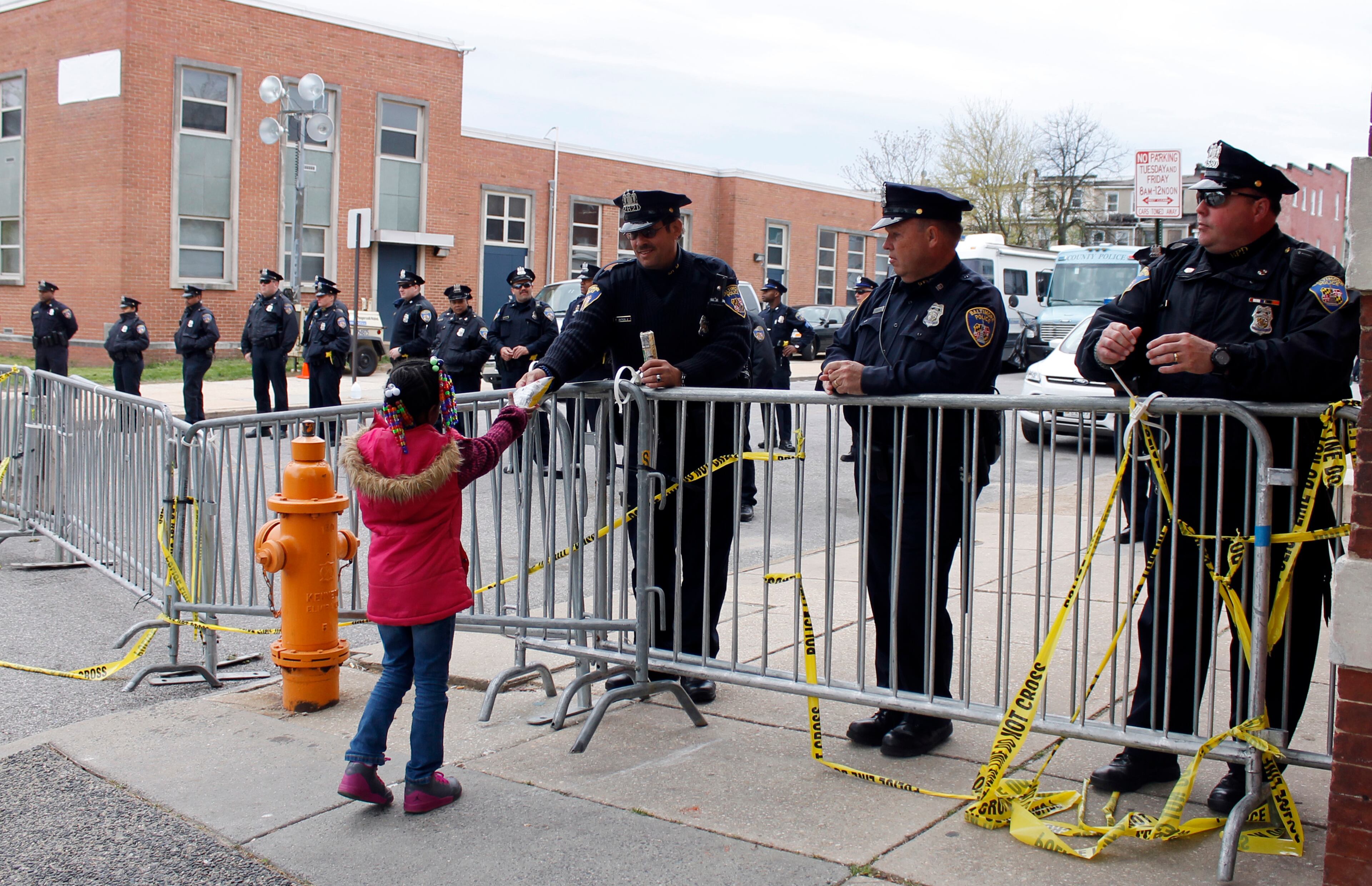A child accepts a gift of a bag of chips from a police officer outside the Western District before a march to City Hall for Freddie Gray, Saturday, April 25, 2015 in Baltimore. Gray died from spinal injuries about a week after he was arrested and transported in a police van. (AP Photo/Skip Foreman)