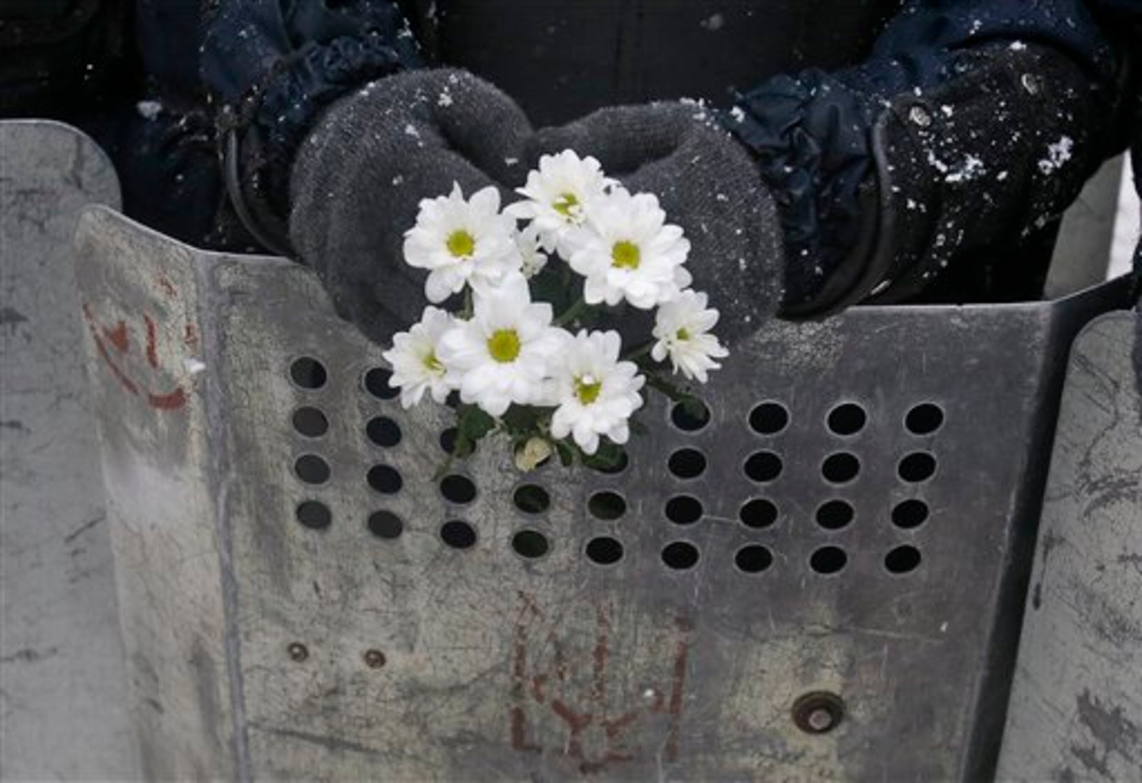 A Ukrainian riot police officer holds a bunch of white flowers given by a protester while blocking the road next to Pro-European Union activists gathered on the Independence Square in Kiev, Ukraine, Monday, Dec. 9, 2013. The policemen, wearing helmets and holding shields, formed a chain across Kiev�s main street outside the city building. Organizers called on protesters to vacate the city hall and the other building which the opposition had used as its headquarters. (AP Photo/Sergei Grits)