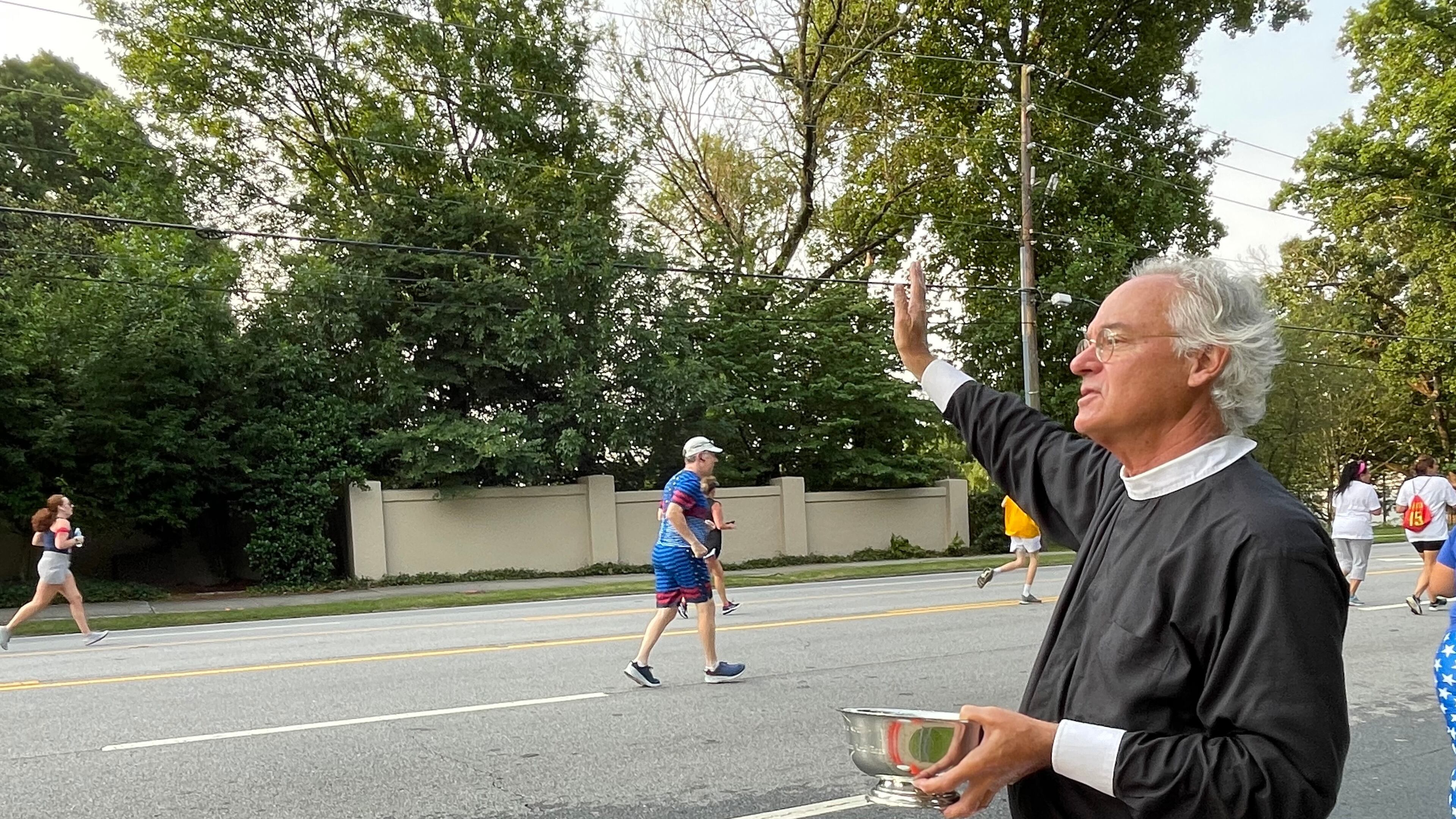 The Rev. Sam Candler of the Cathedral of St. Philip blessed runners with holy water. (Photo: Anjali Huynh/AJC)