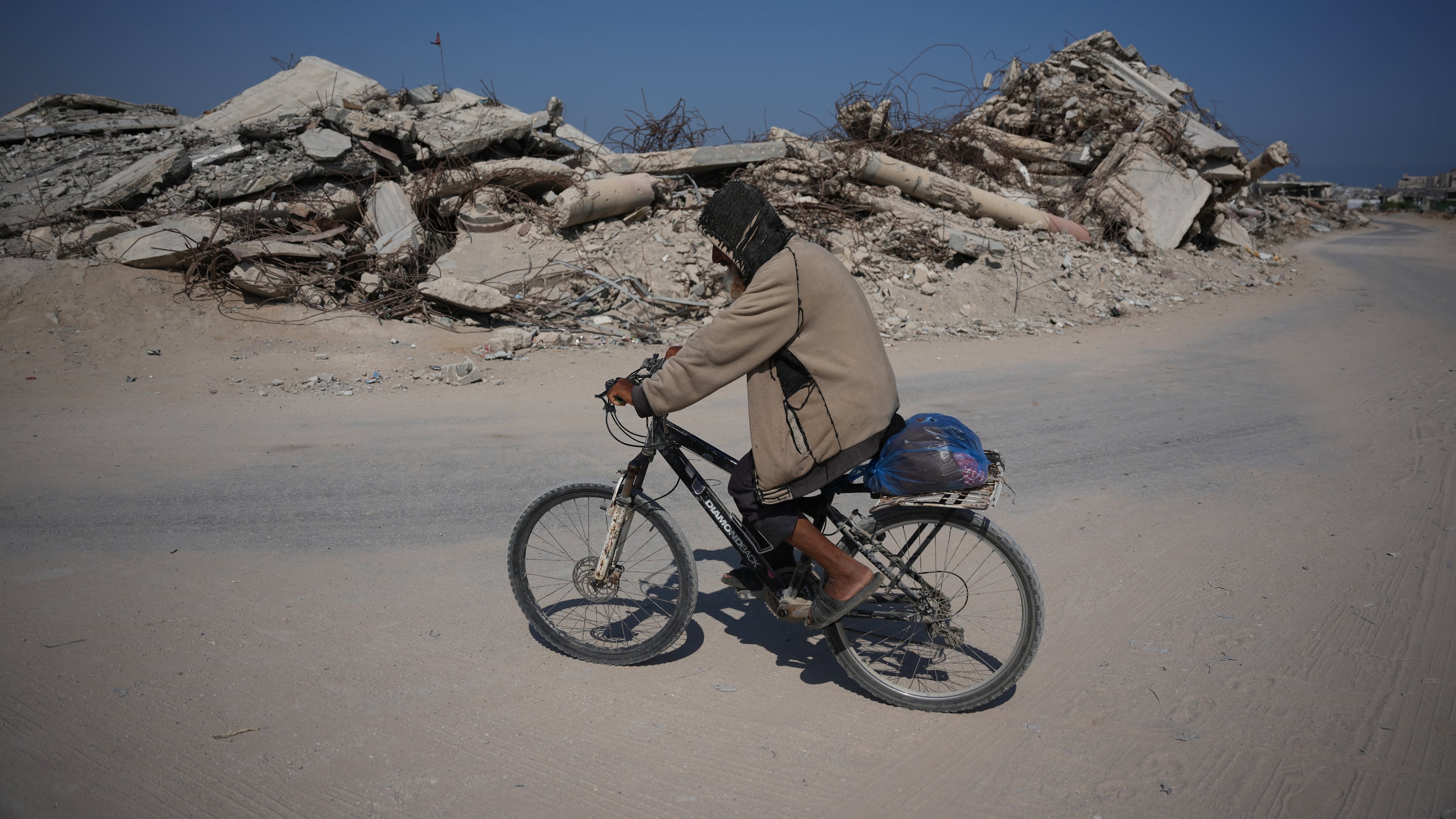 A Palestinian man rides his bicycle by the rubble of buildings that were destroyed during the Israel Hamas war, in Khan Younis, southern Gaza Strip, Friday, July 31, 2026. (AP Photo/Abdel Kareem Hana)